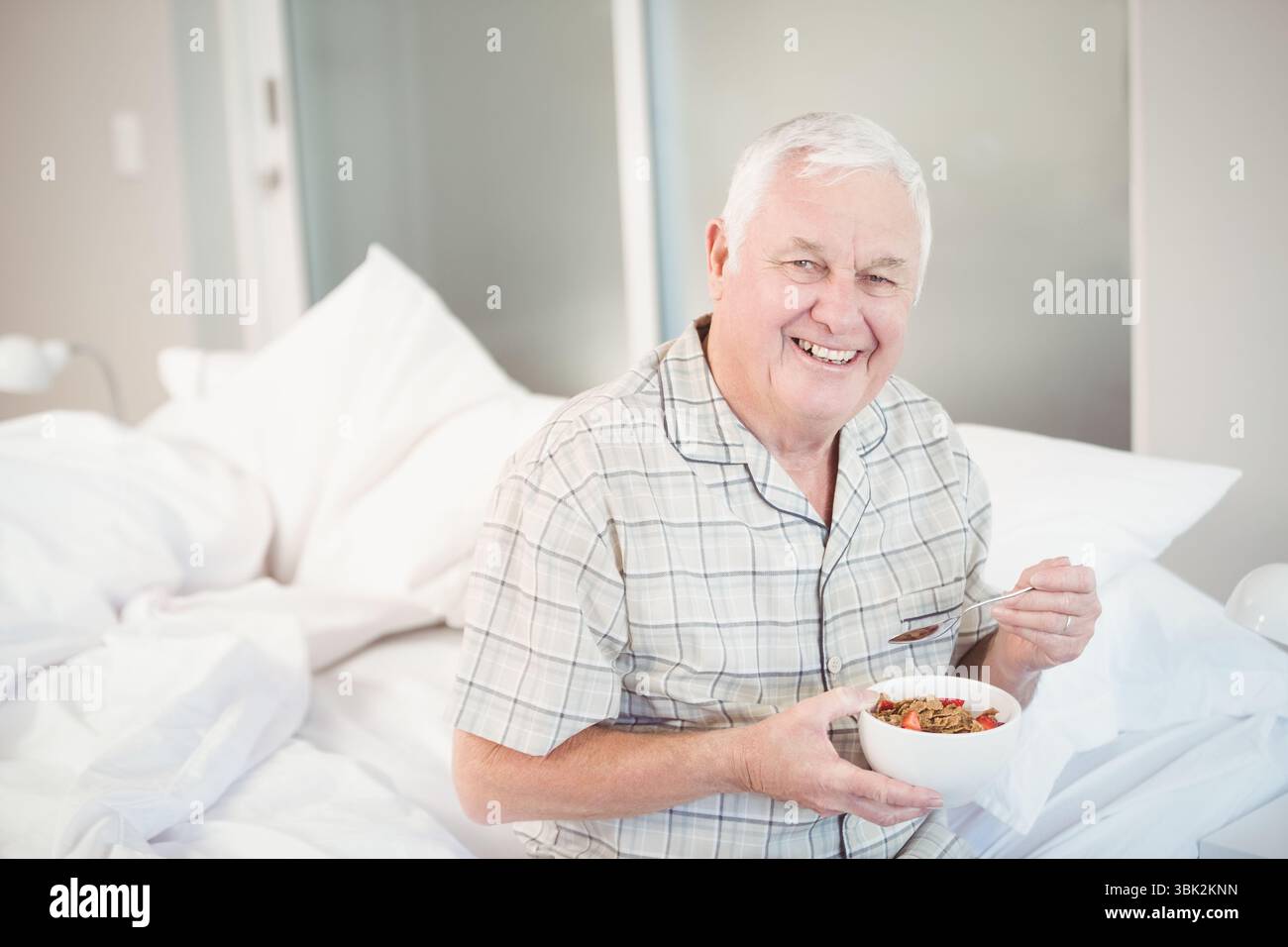 bol contenant du granola et des fruits reposant sur le lit avec oreillers et lampe près des portes en verre dépoli Banque D'Images