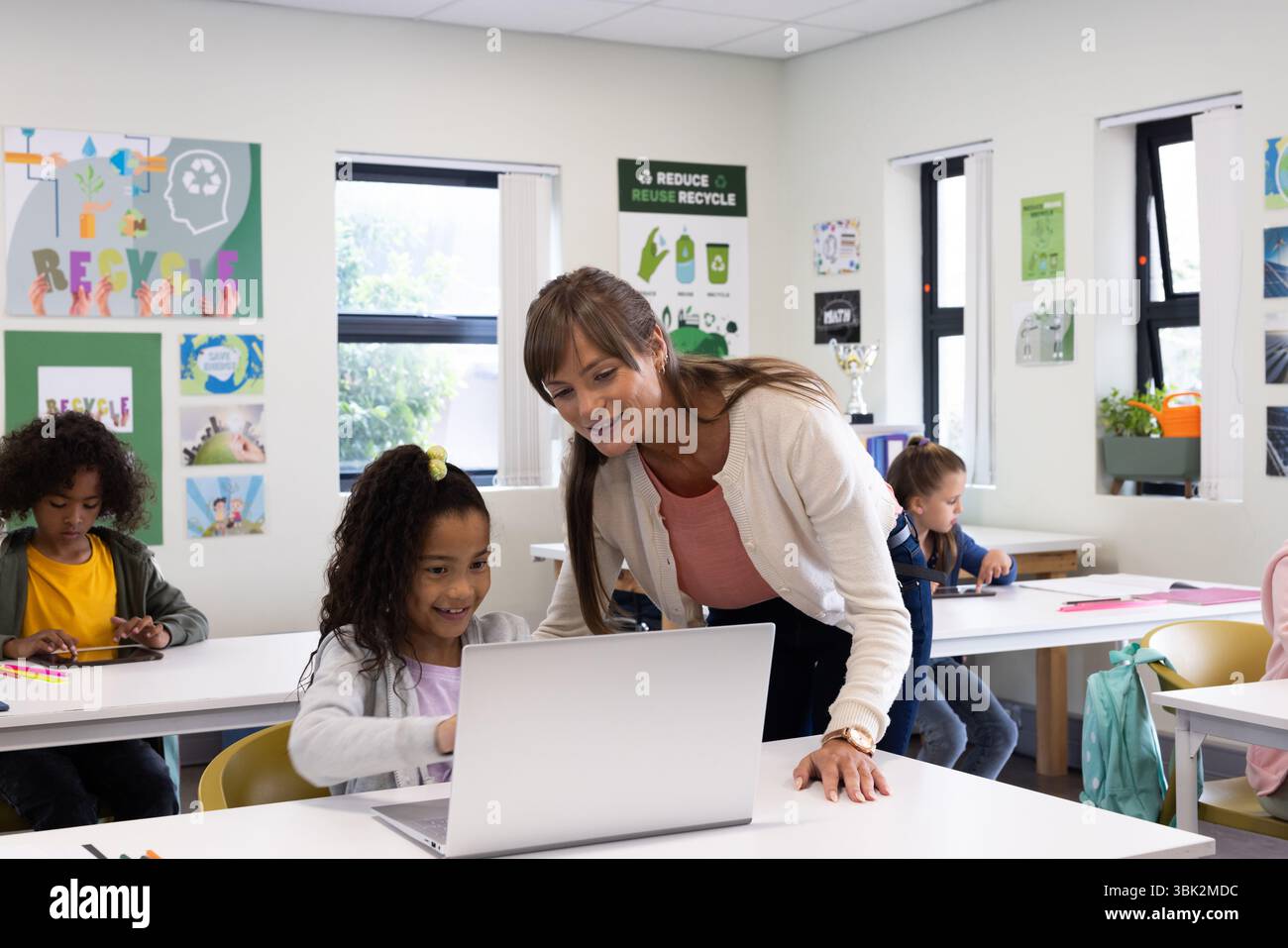 À l'école, enseignante aidant la fille avec un ordinateur portable, favorisant l'apprentissage et l'engagement Banque D'Images