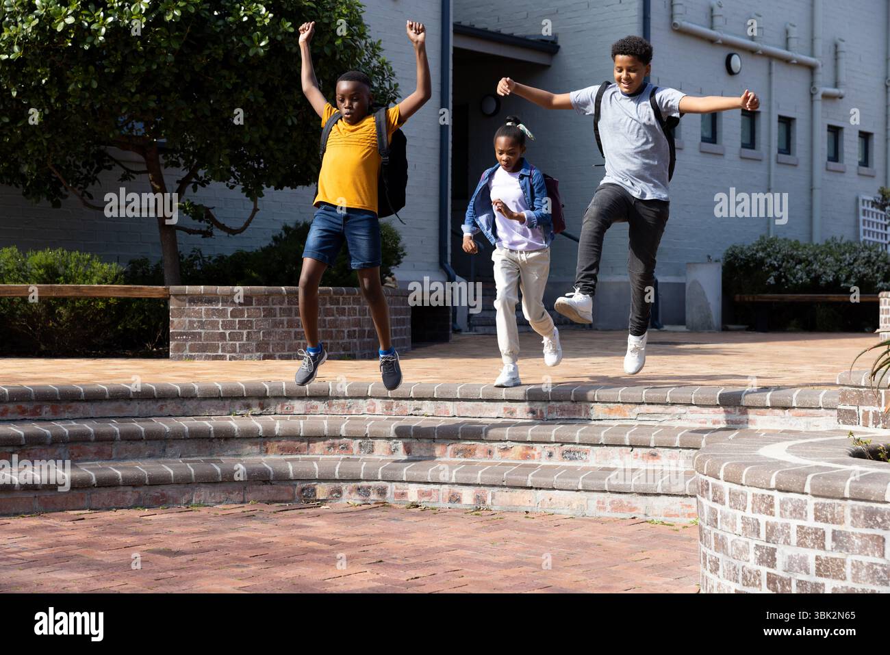 Étudiants joyeux et diversifiés avec des sacs à dos sautant sur les marches de l'école, profitant du plaisir en plein air Banque D'Images