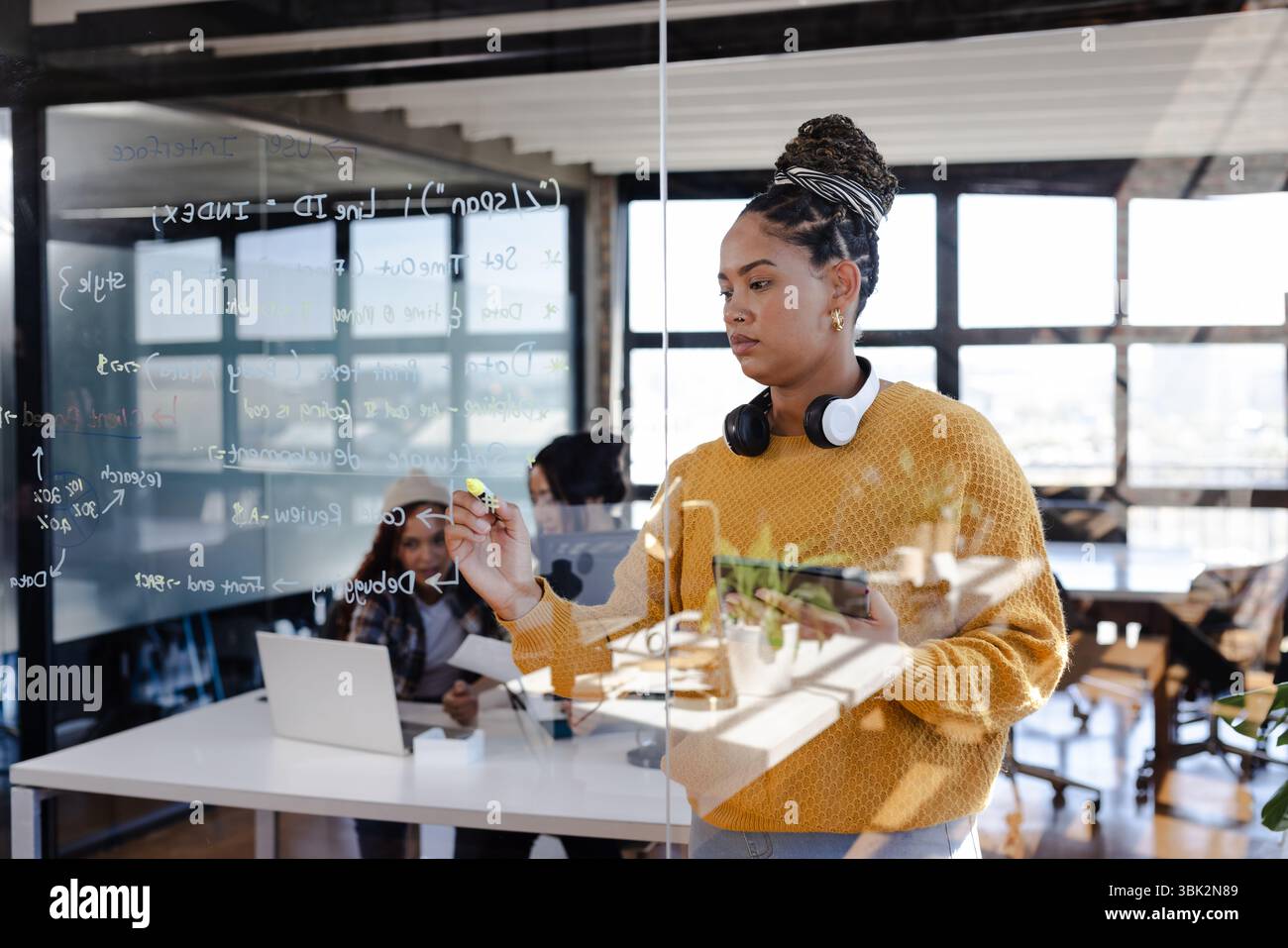 Femme confiante écrivant code sur panneau de verre dans un cadre de bureau moderne Banque D'Images