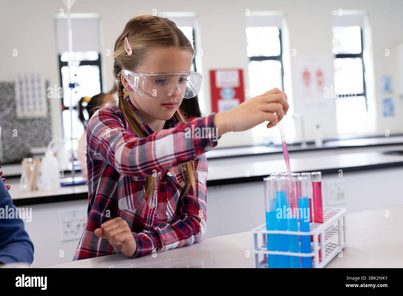 Fille dans le laboratoire de l'école menant des expériences avec des éprouvettes, portant des lunettes de sécurité Banque D'Images
