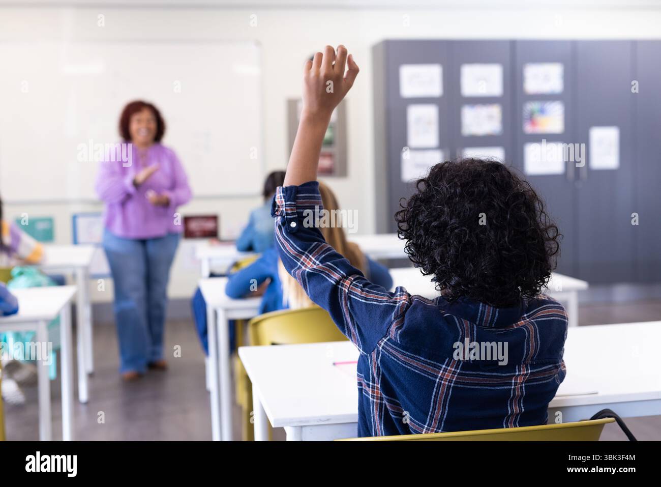Élève levant la main en classe tandis que l'enseignante s'engage avec divers élèves, à l'école Banque D'Images