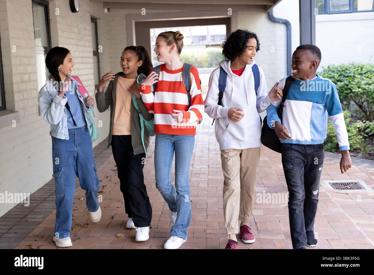 Groupe diversifié d'étudiants marchant et riant ensemble à l'extérieur du bâtiment de l'école Banque D'Images