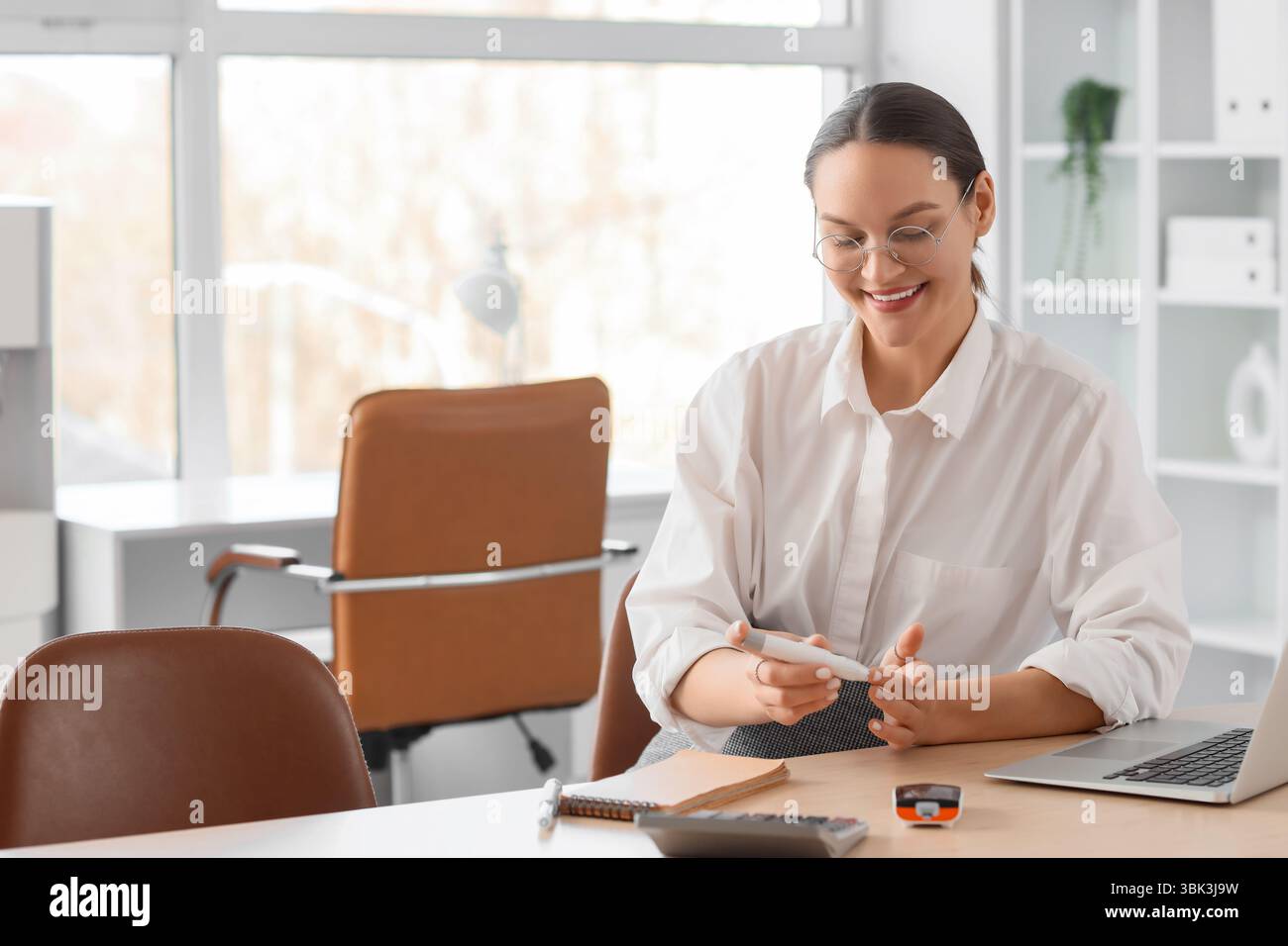 Jeune femme d'affaires enceinte avec diabète gestationnel utilisant le stylo lancette dans le bureau Banque D'Images