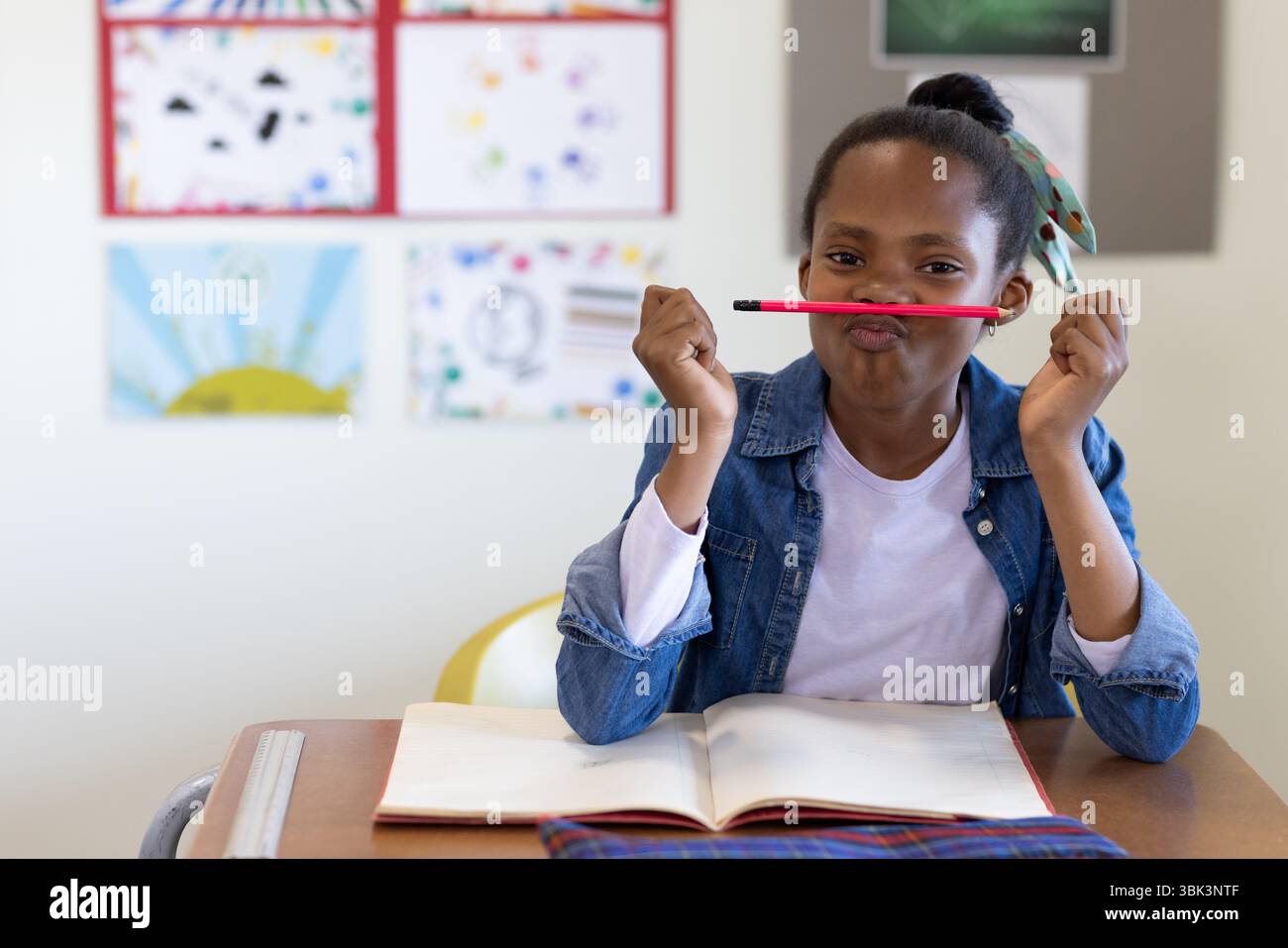 En classe, fille ludique équilibrant le crayon sur la lèvre, profitant de vacances scolaires Banque D'Images