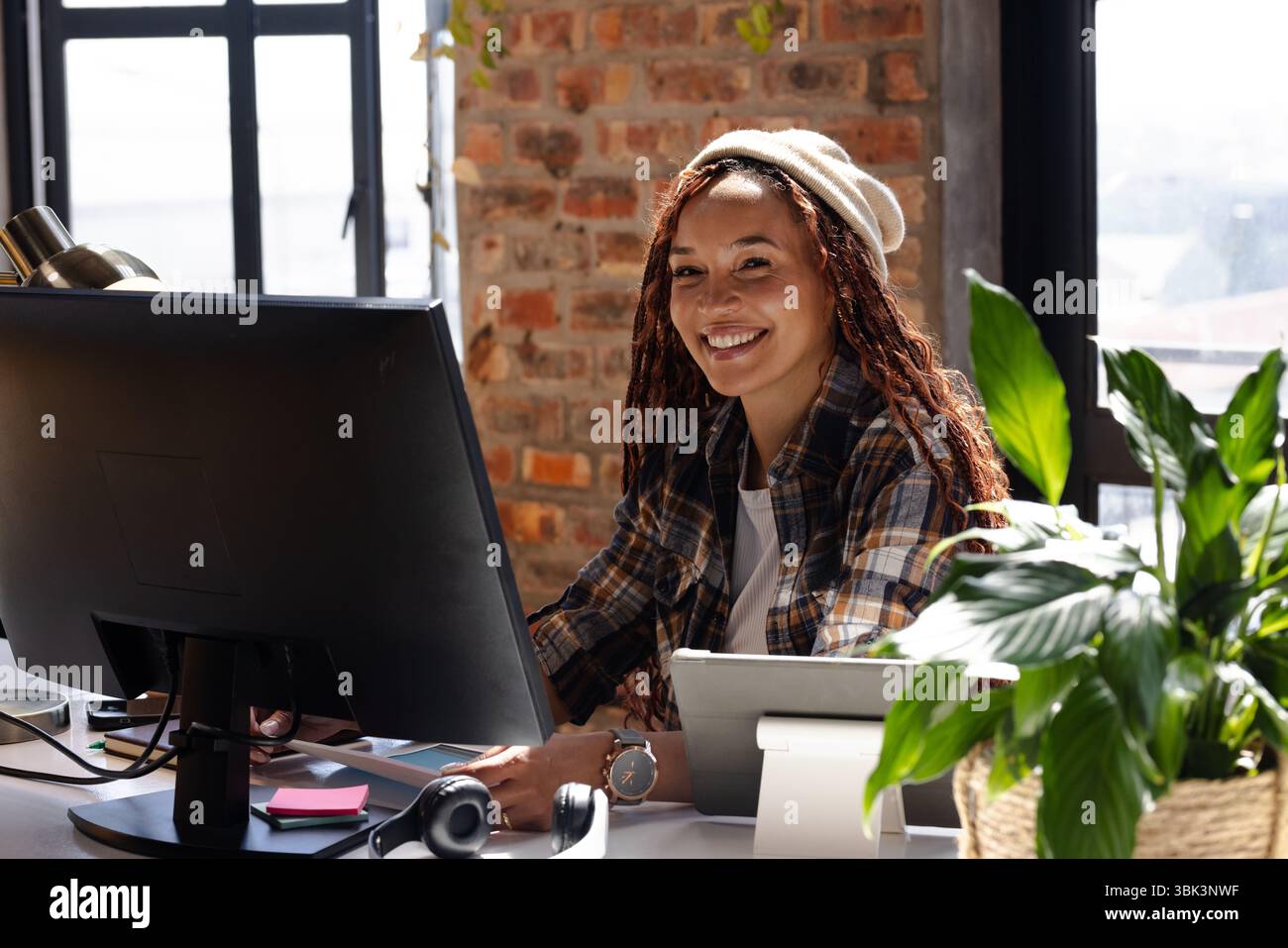 Femme souriante codant au bureau avec ordinateur et plantes dans le bureau moderne Banque D'Images