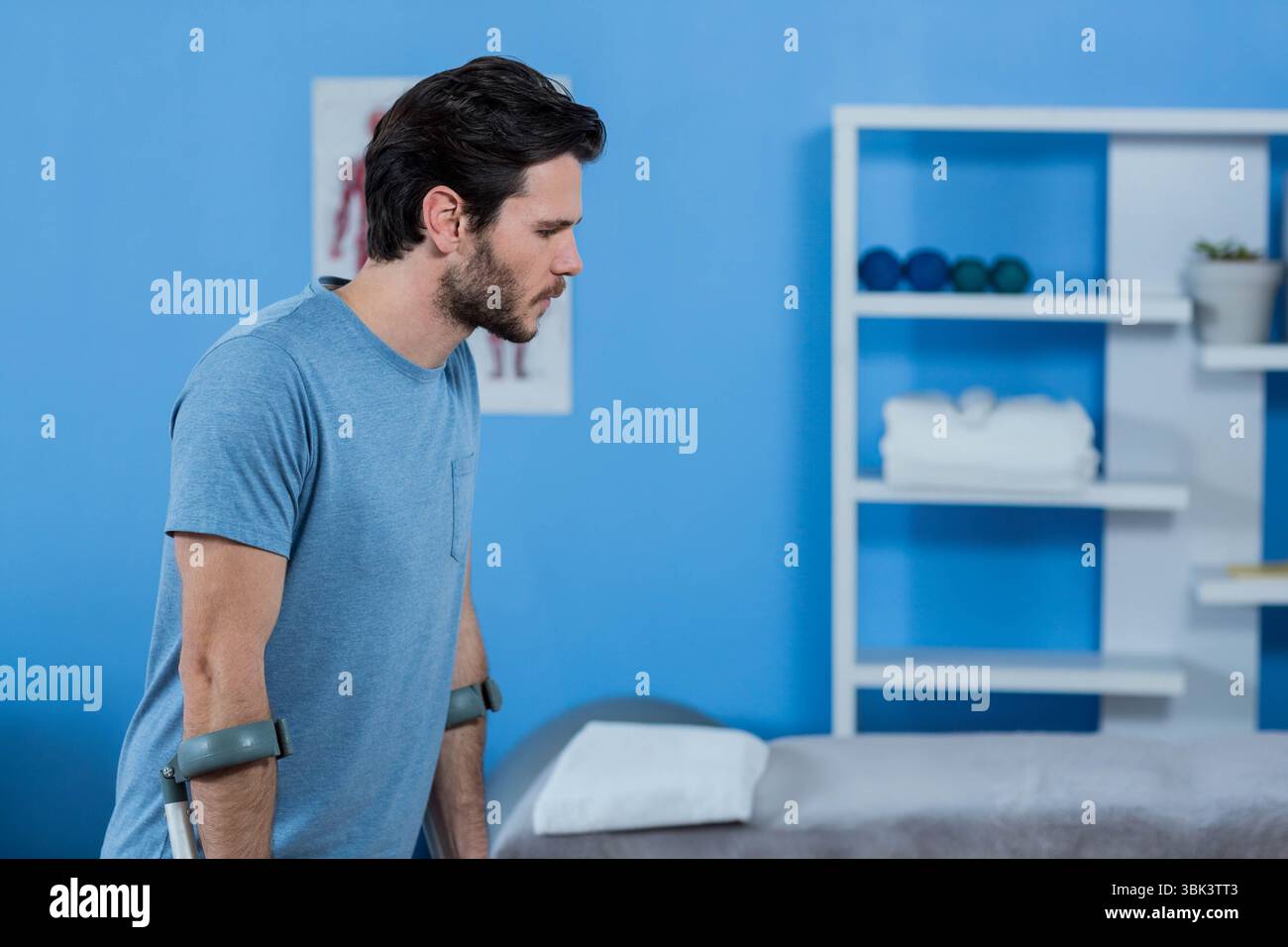 Patient masculin appuyé sur des béquilles d'avant-bras dans la salle de thérapie avec poids et serviettes, espace de copie Banque D'Images