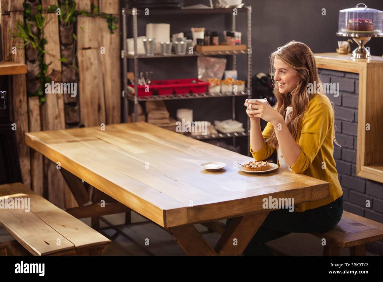 Tasse de café blanc et pâtisserie sur l'assiette reposant à la table commune en bois clair dans le café industriel rustique Banque D'Images