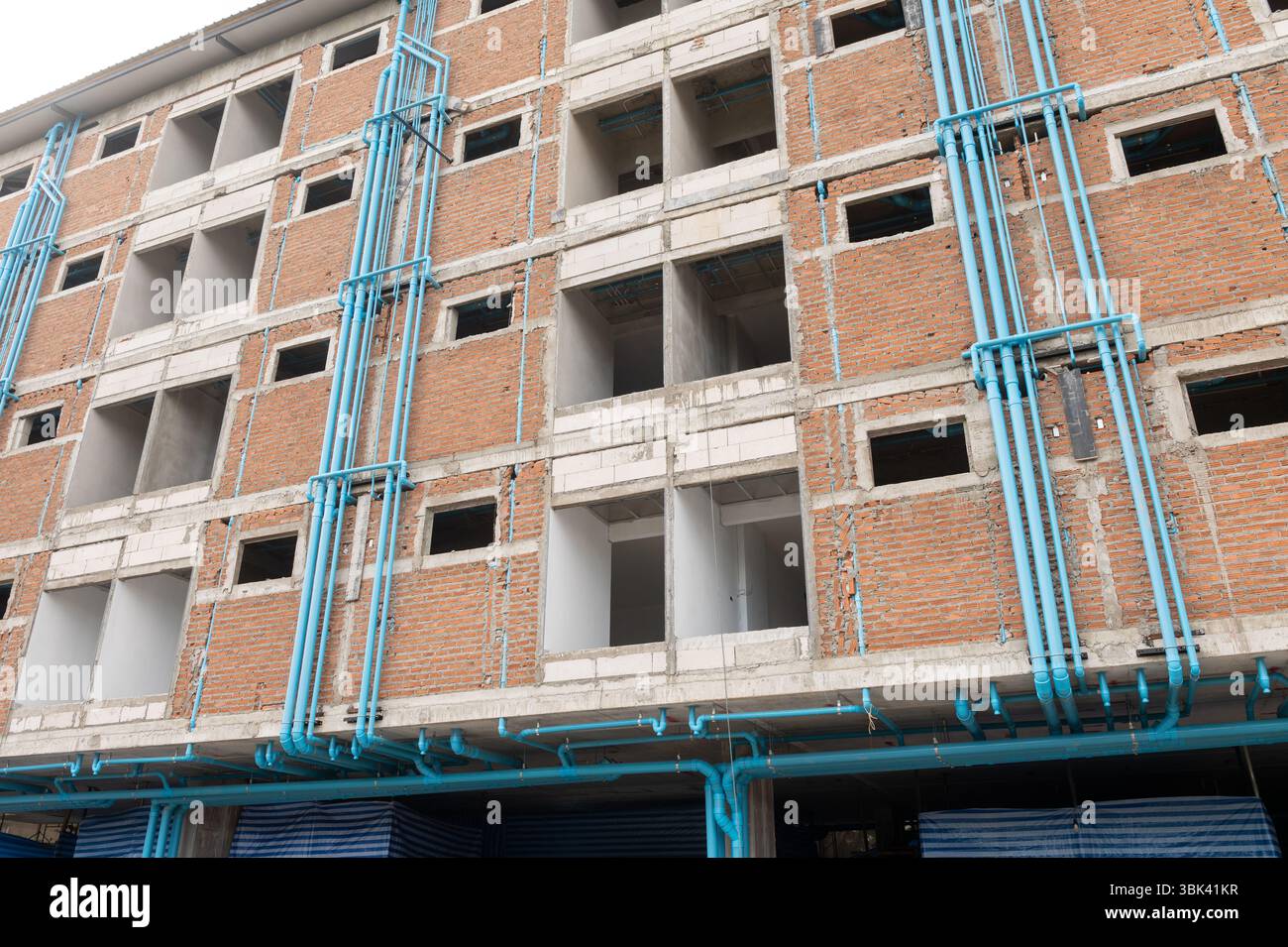 Bâtiment non fini en construction avec murs de briques rouges apparents et tuyaux de plomberie en PVC bleu visible Banque D'Images