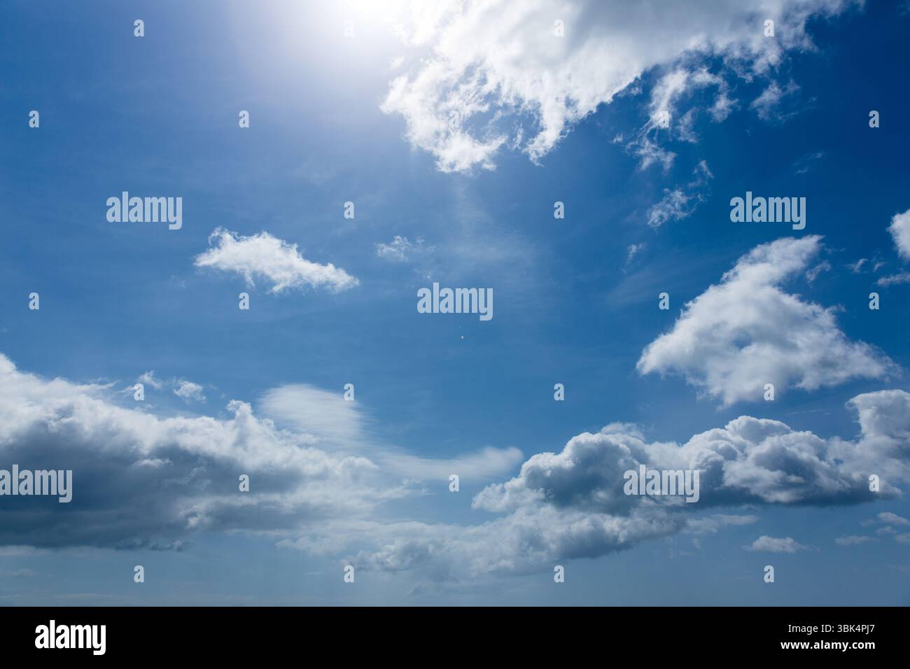 De grands nuages de cumulus flottent à travers le ciel plat avec des reflets ensoleillés et des stries sinueuses Banque D'Images