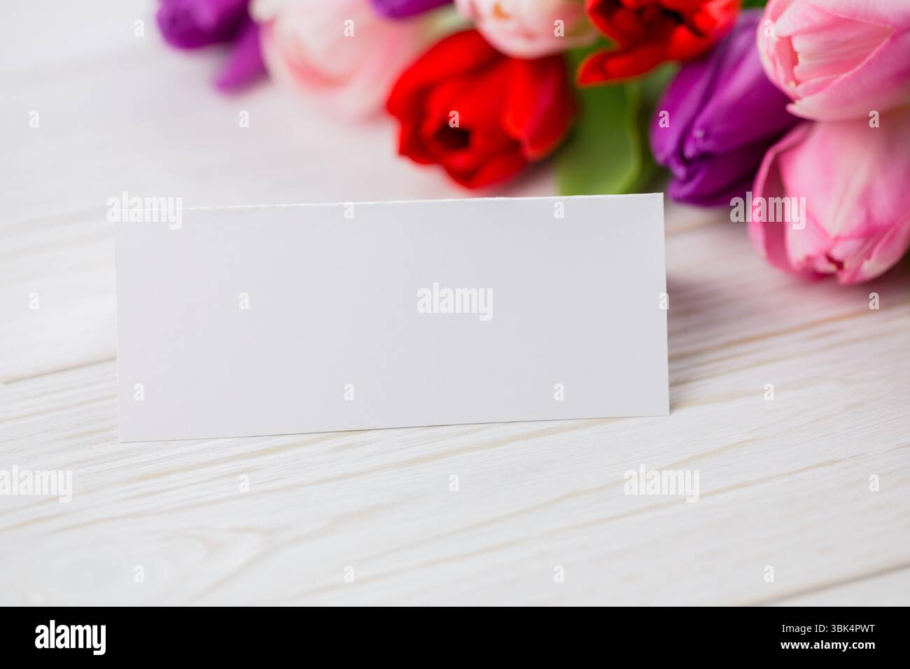 L'illustration de conception plate montre une carte blanche vierge sur une table en bois avec des tulipes roses, espace de copie Banque D'Images