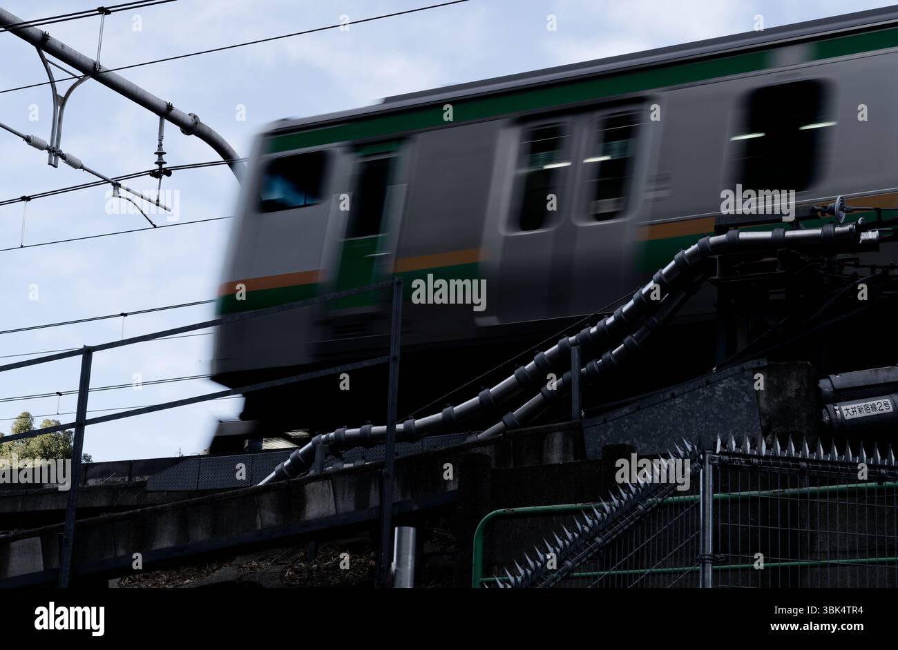 Le train JR East roule le long de voies surélevées, passant devant des lignes électriques et des barrières renforcées Banque D'Images