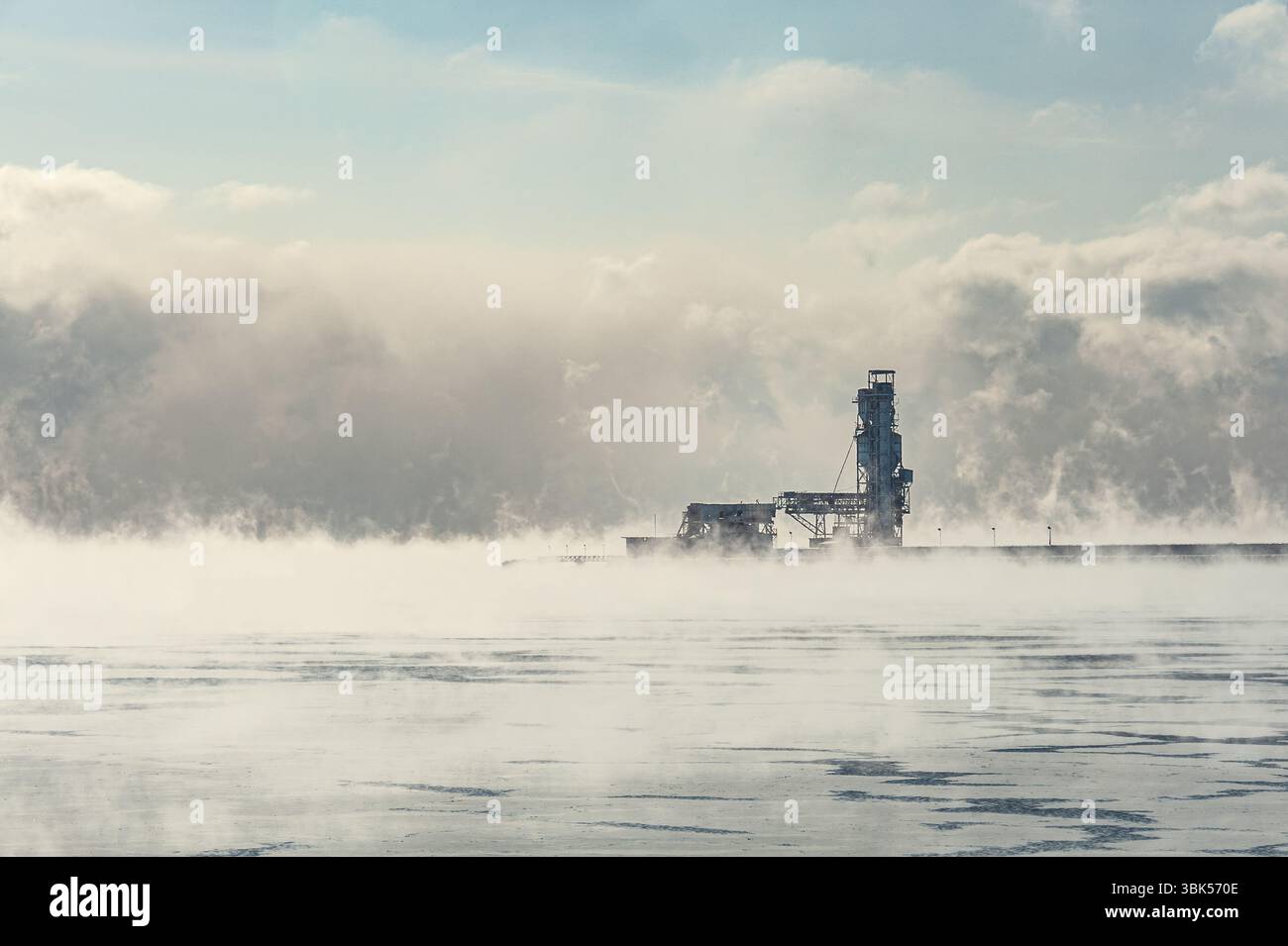 Jetée industrielle et tour de chargement entourée de brume de lac par un matin froid. Scène atmosphérique avec glace et vapeur. Banque D'Images