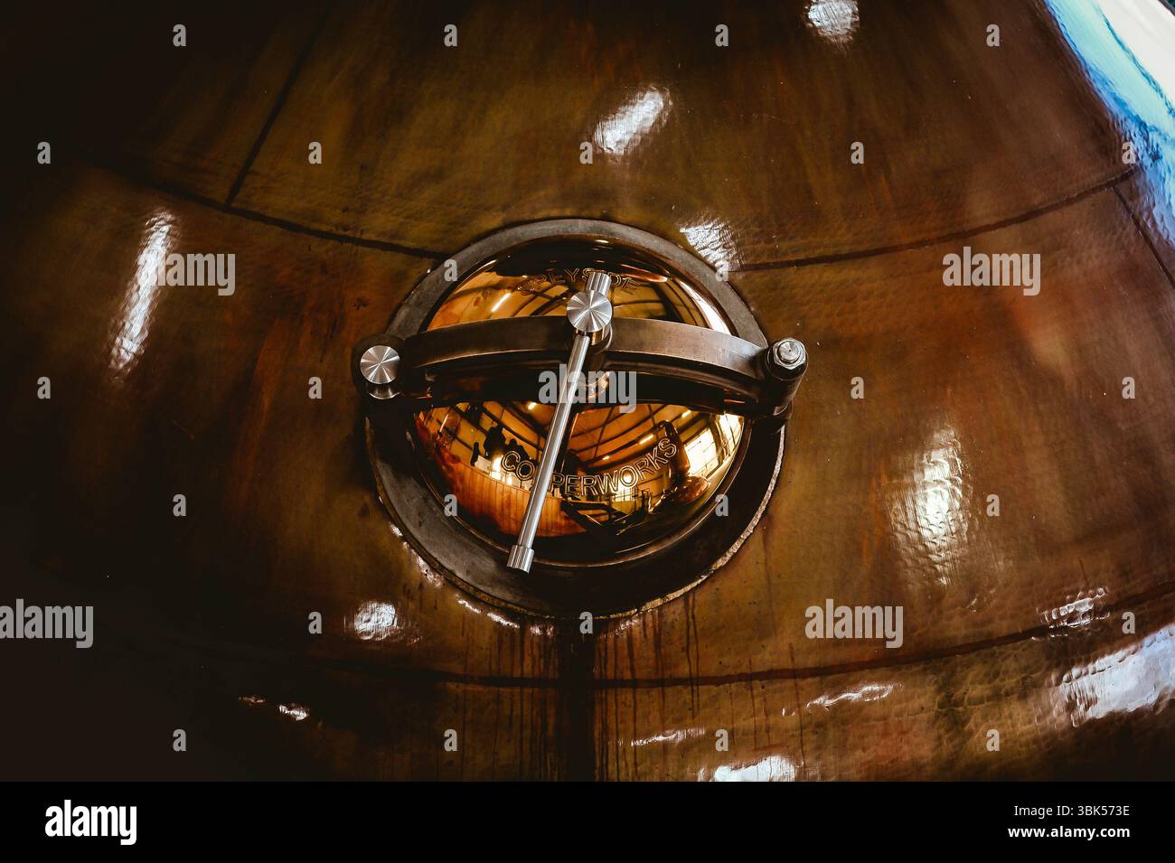 Gros plan d'un pot en cuivre avec trappe principale et poignée, utilisé dans la distillation traditionnelle de whisky. Surface polie réfléchissant l'intérieur de la distillerie. Banque D'Images