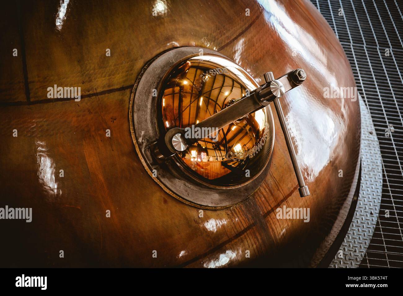 Gros plan d'un pot en cuivre avec trappe principale et poignée, utilisé dans la distillation traditionnelle de whisky. Surface polie réfléchissant l'intérieur de la distillerie. Banque D'Images