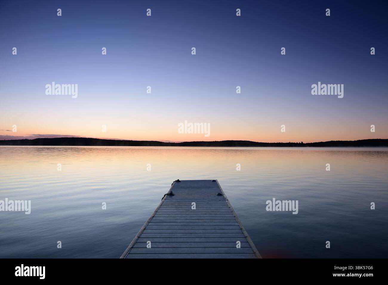 Lac calme au lever du soleil avec quai vide menant à l'eau calme. Scène matinale paisible dans la nature. Banque D'Images
