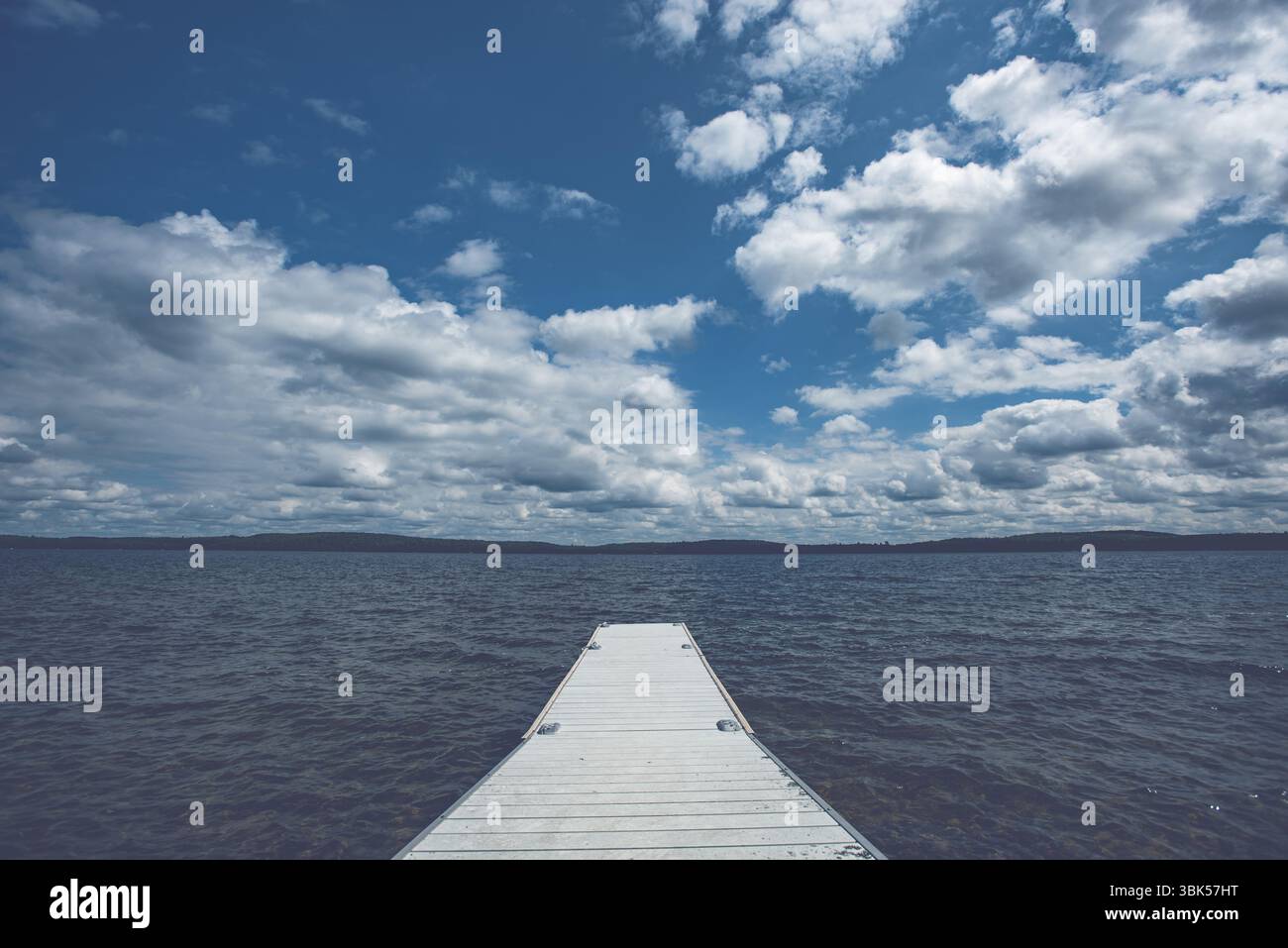 Quai blanc s'étendant dans un large lac nord sous un ciel spectaculaire rempli de cumulus nuages. Météo estivale et eau libre dans le pays des chalets. Banque D'Images