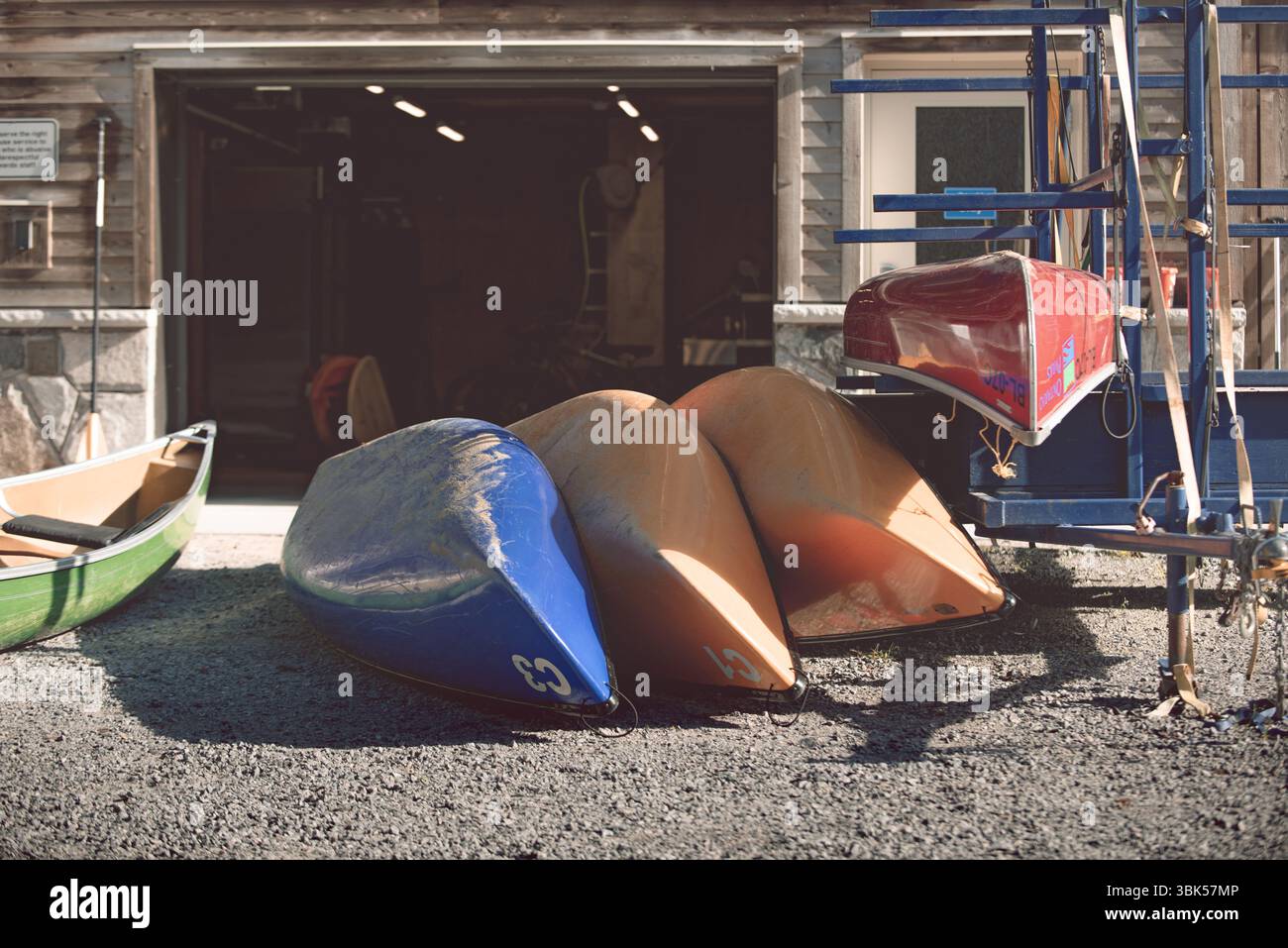 Canoës colorés stockés à l'envers à l'extérieur d'un hangar à bateaux sur une allée de gravier. Lumière tôt le matin et calme scène saisonnière de bord de mer. Banque D'Images