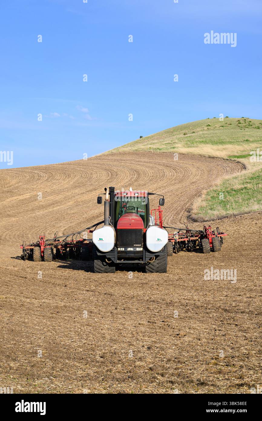 Palouse, WA, États-Unis - 7 mai 2025 ; tracteur agricole dans un paysage de collines partiellement labourées Banque D'Images
