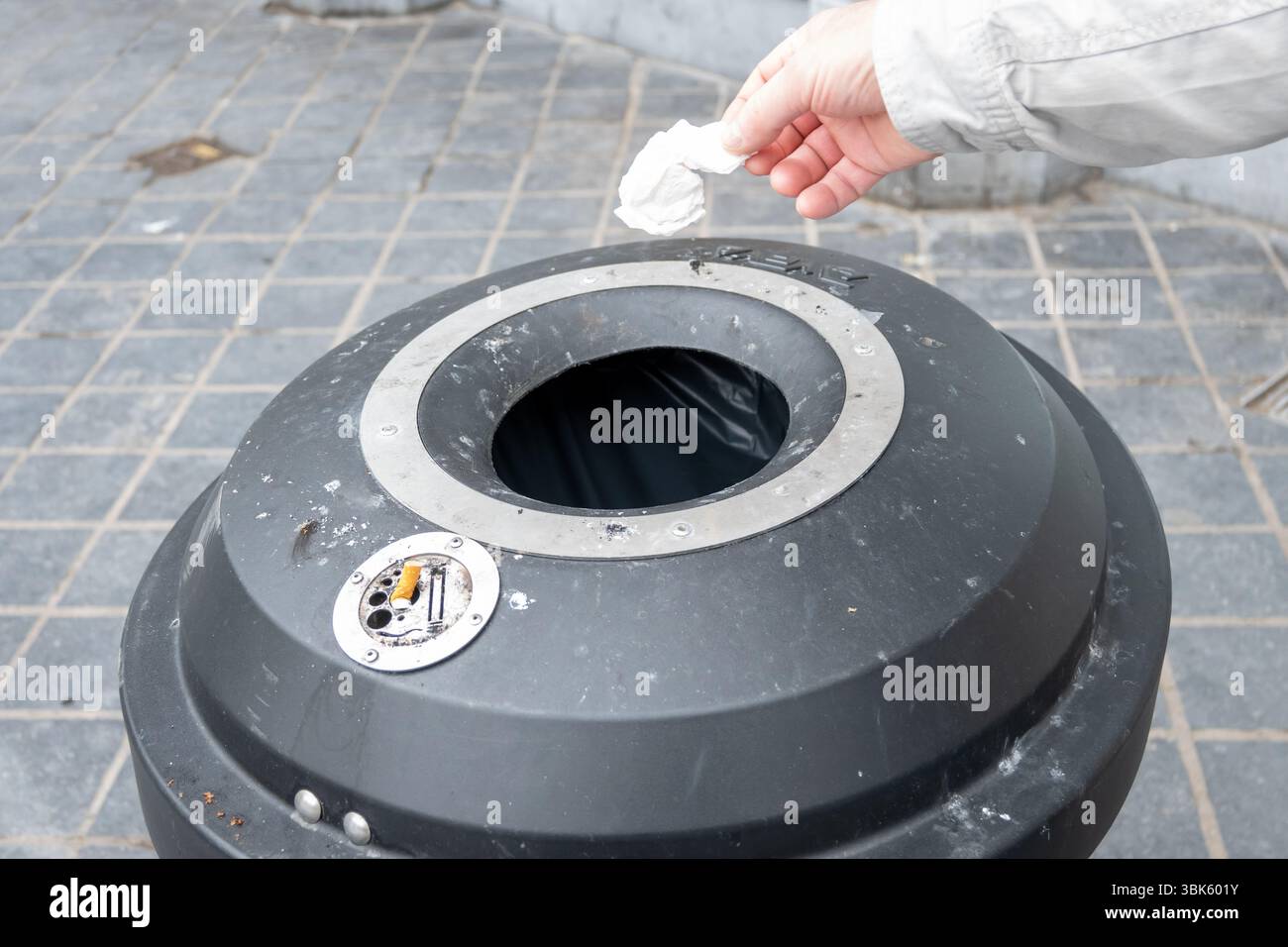 Main de la personne jetant une serviette en papier froissée dans la poubelle. Poubelle en métal dans la rue. L'hygiène en ville. Banque D'Images