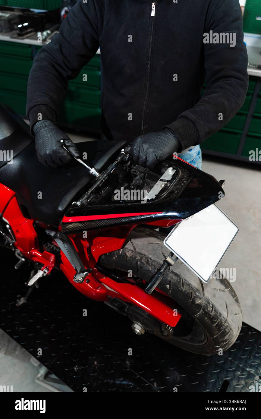 La dépose du siège de moto est essentielle pour contrôler le circuit électrique. Le technicien dépose soigneusement le siège de la moto à l'aide d'outils pour accéder à l'int Banque D'Images