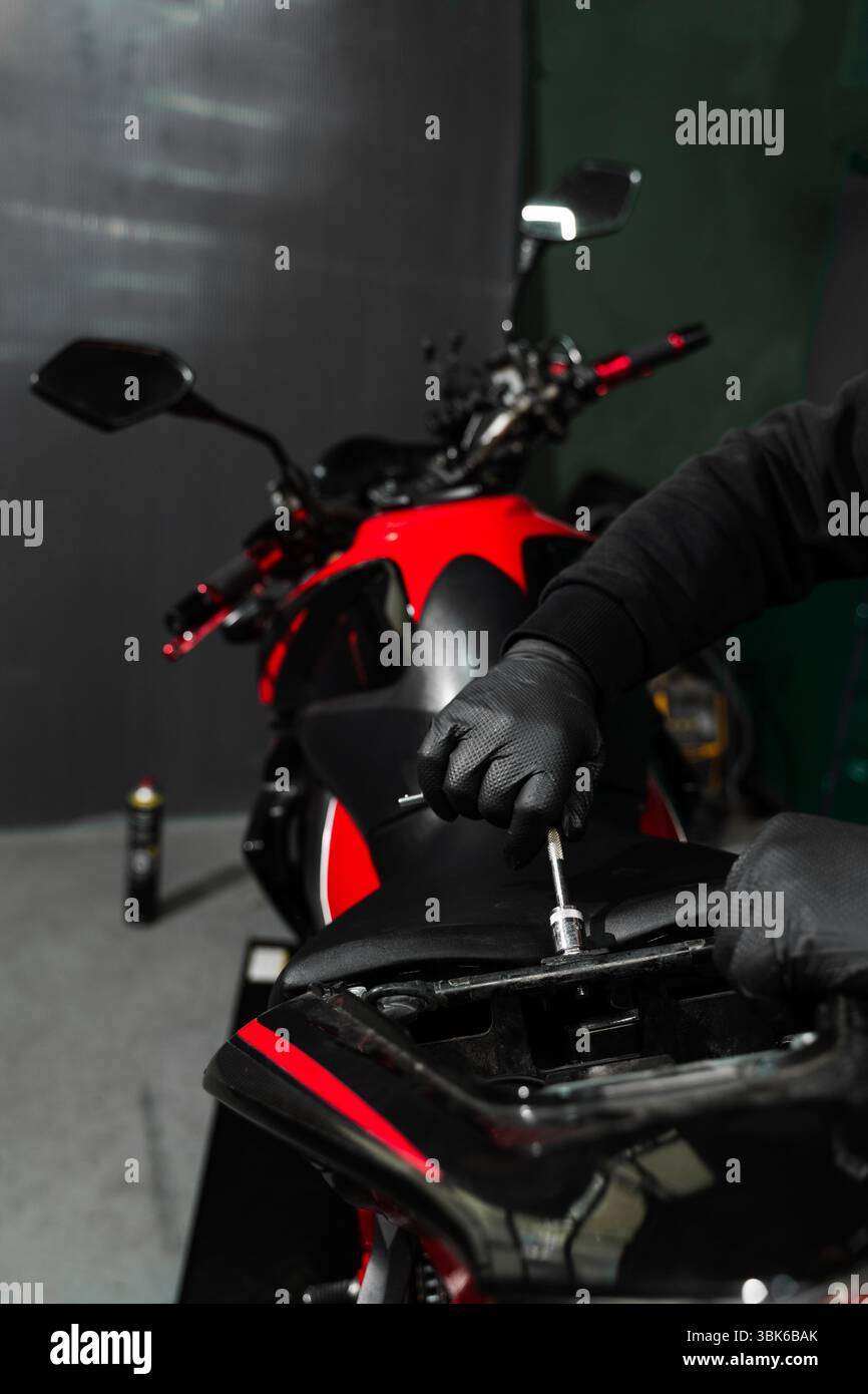 Le technicien dépose soigneusement le siège de moto à l'aide d'outils pour accéder aux composants internes à des fins de diagnostic. La dépose du siège de moto est essentielle pour i Banque D'Images