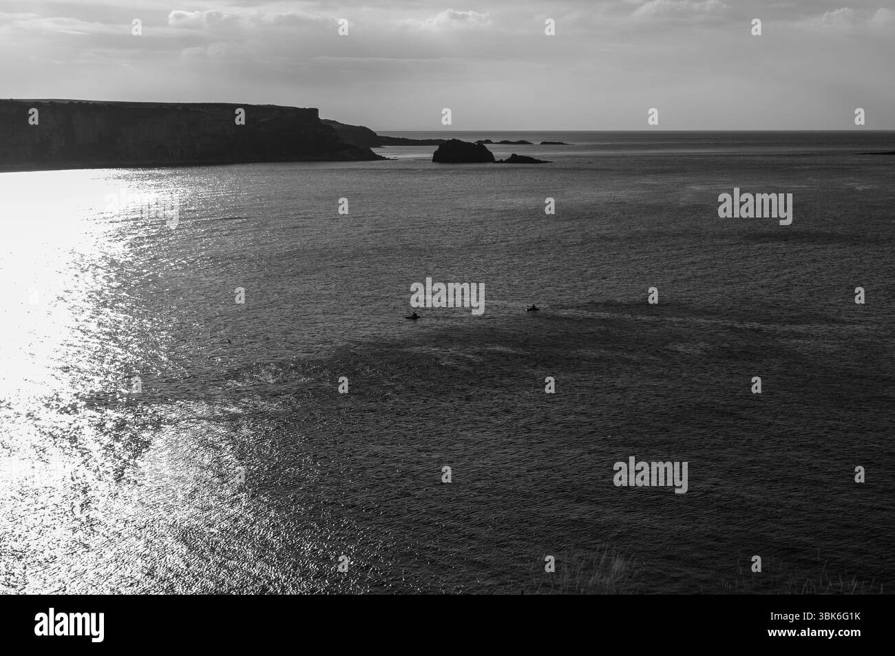 Photo en noir et blanc d'un plan d'eau avec un rivage rocheux. L'eau est calme et le ciel nuageux Banque D'Images