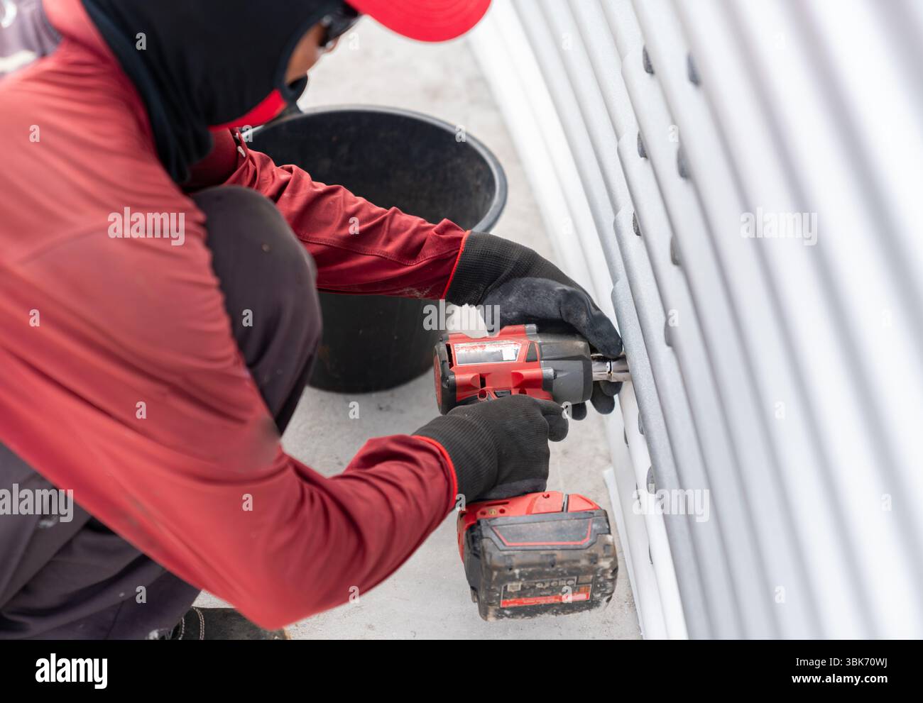 Le travailleur utilise une clé à chocs sans fil pour serrer les boulons sur la paroi du réservoir en tôle sur le site d'installation. Banque D'Images