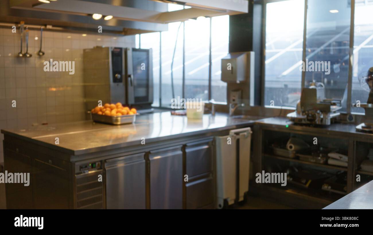 Cuisine moderne du restaurant avec comptoir en acier inoxydable, oranges fraîches dans un plateau, grandes fenêtres et éclairage bokeh flou de la hauteur Banque D'Images