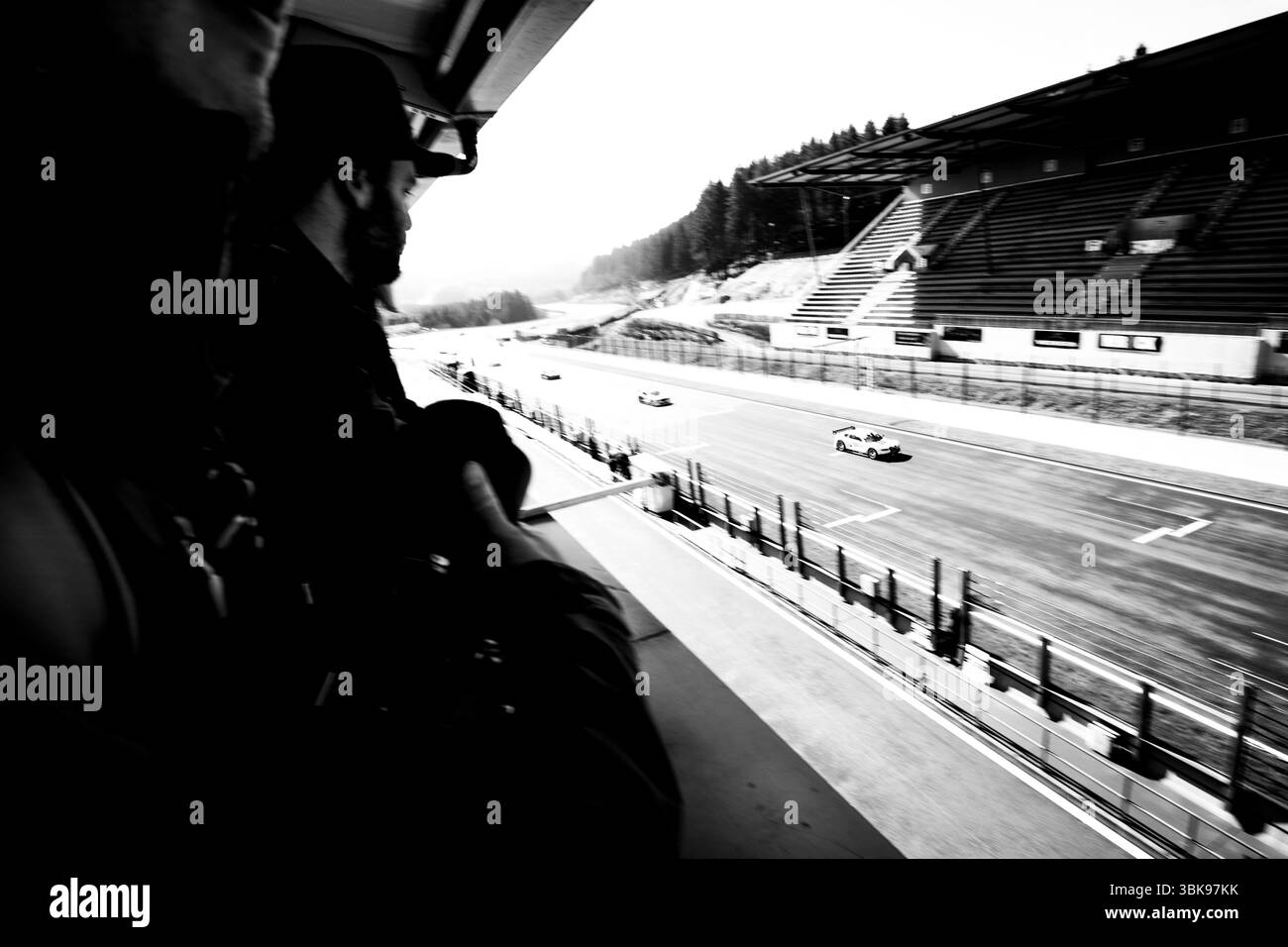 Un cliché noir et blanc saisissant capture la vue exaltante d'une course de sports mécaniques depuis une tribune. Une silhouette au premier plan ajoute de la profondeur. Banque D'Images