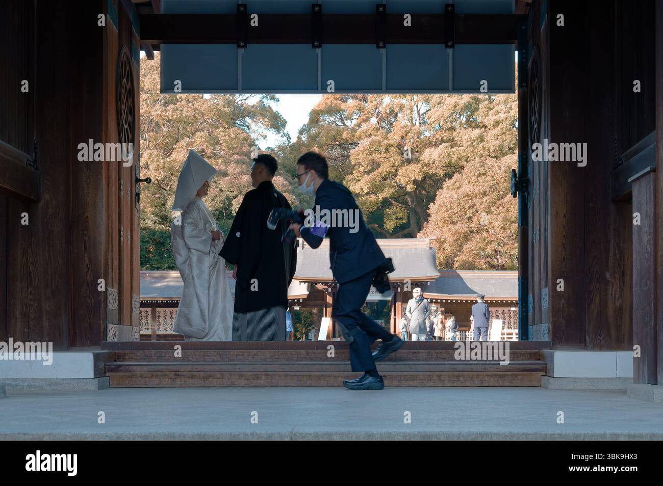Le photographe se précipite pour capturer le moment parfait alors qu'une mariée et un marié se tiennent debout sous une porte en bois du sanctuaire Meiji Jingu Banque D'Images