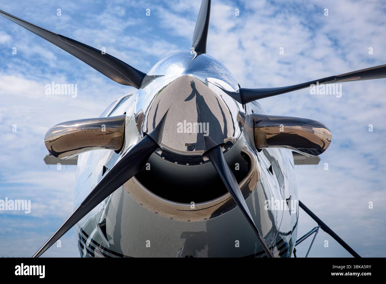 Gros plan extrême du nez et du moyeu d'hélice d'un avion turbopropulseur, avec des reflets de pales et des détails sous un ciel bleu. Banque D'Images