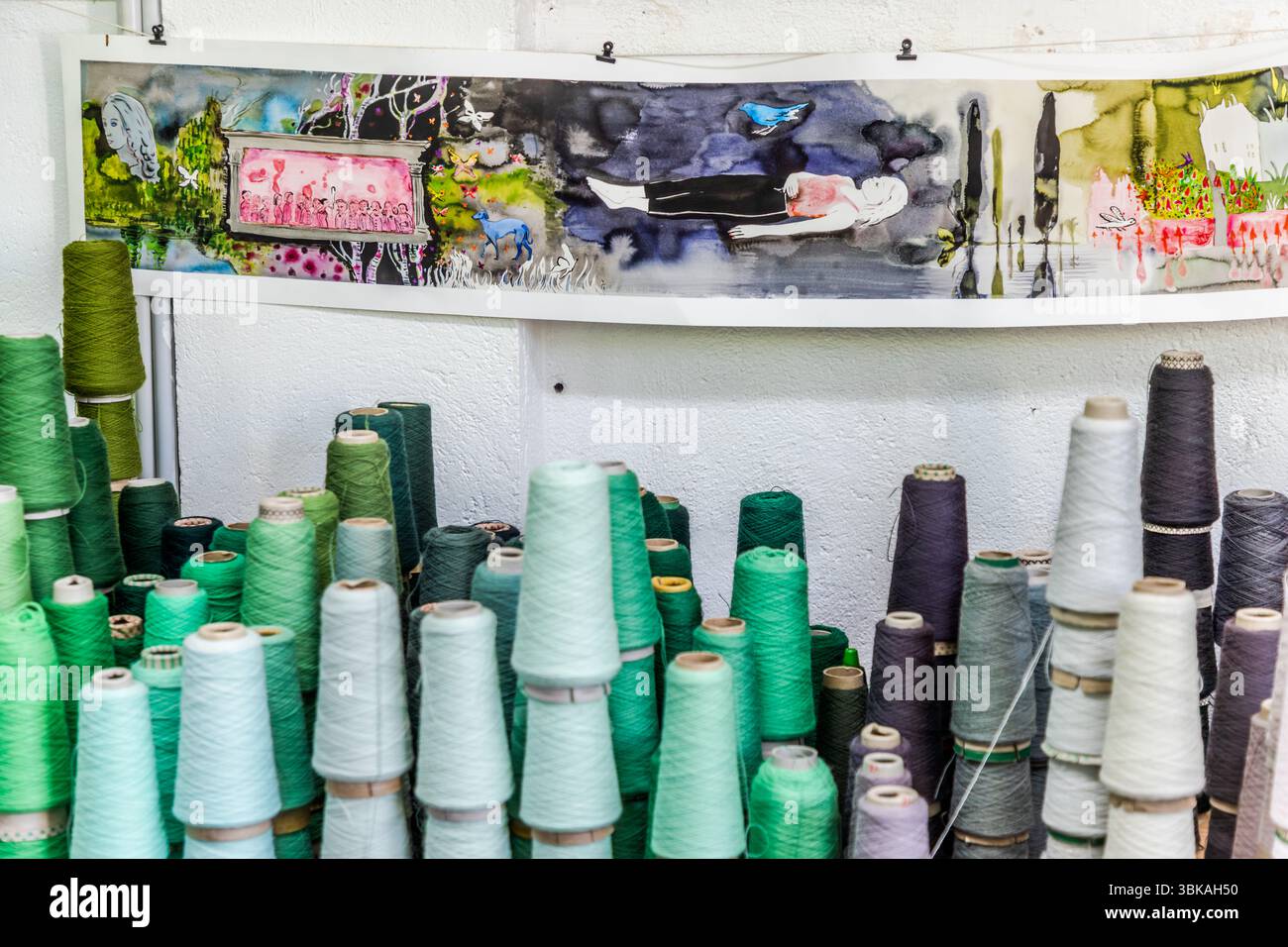 Une section du design de la tapisserie « Hommage à George Sand » par Françoise Pétrovitch est suspendue au-dessus des fils de laine dans l'atelier de tissage Robert Four (Manufacture Robert Four) sur la Rue Madeleine à Aubusson, Creuse, Nouvelle-Aquitaine, France. Dans une sorte de mise en scène théâtrale est représenté le cercle artistique et littéraire qui se réunissait régulièrement chez George Sand. Outre Frédéric Chopin, il comprenait Franz Liszt, Honoré de Balzac, Gustave Flaubert et Eugène Delacroix. La scène teintée de rose est encadrée d'un cadre gris entre des troncs de bouleau blanc et des papillons. Un visage de femme pâle flotte sur le Banque D'Images