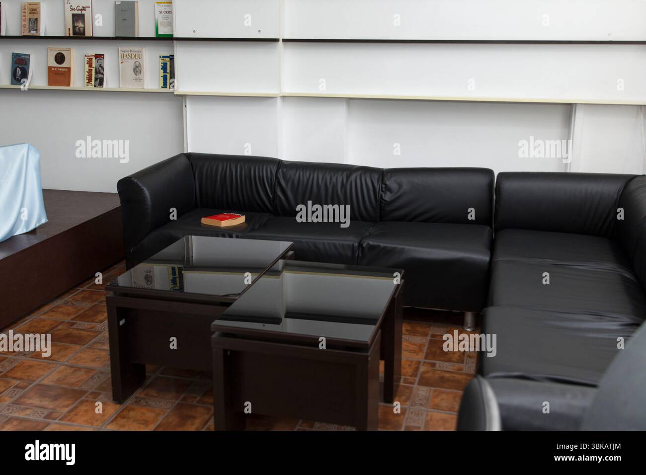 CHISINAU, MOLDAVIE - 14 MARS 2025 ; canapé d'angle en cuir noir avec tables basses en verre dans une salle de bibliothèque confortable avec des livres sur des étagères murales blanches, moderne Banque D'Images