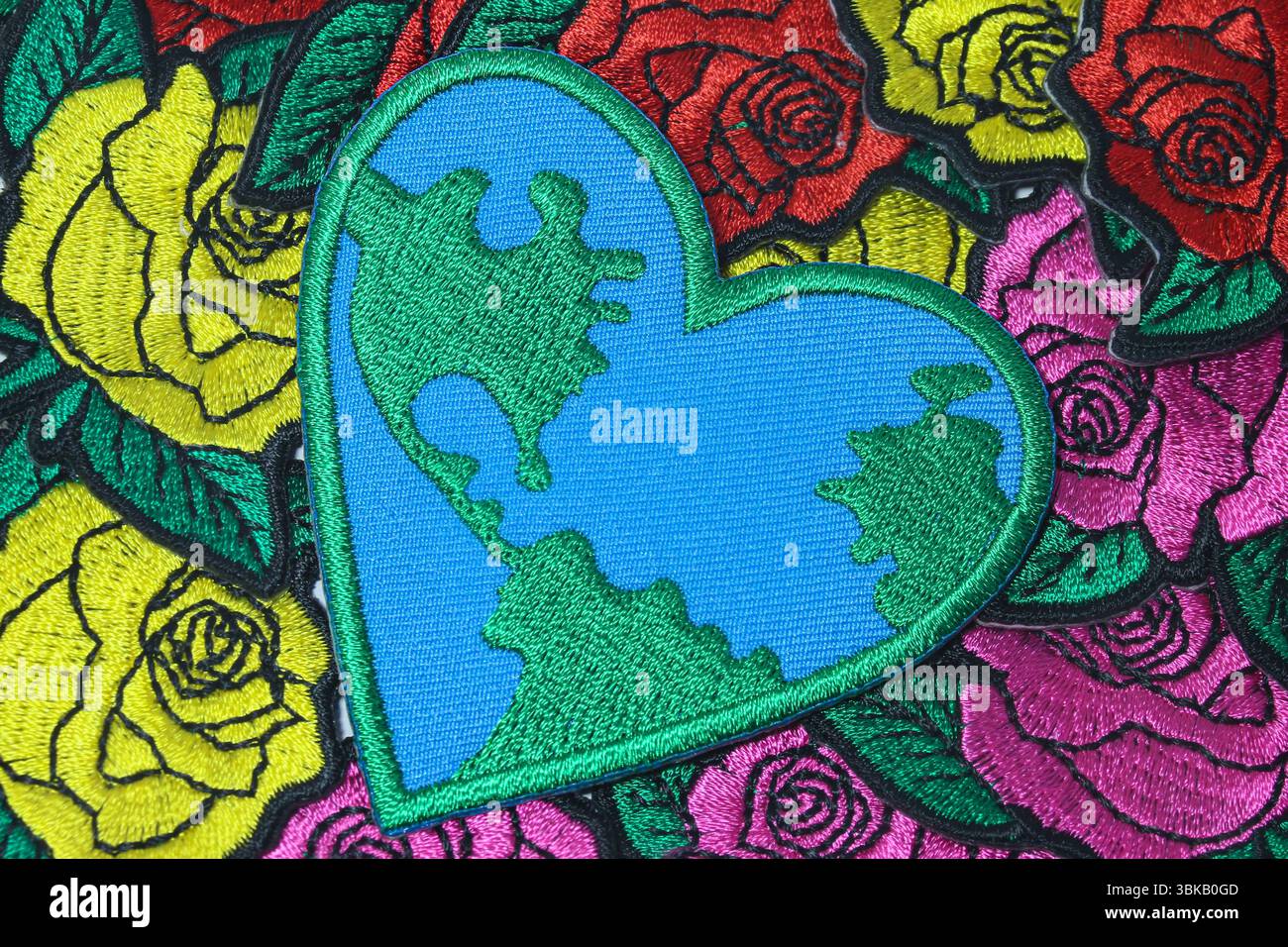 Coeur brodé avec carte du monde sur tissu à motif rose. Art écologique pour le jour de la Terre, symbolisant l'amour pour la planète et la sensibilisation au réchauffement climatique. Banque D'Images