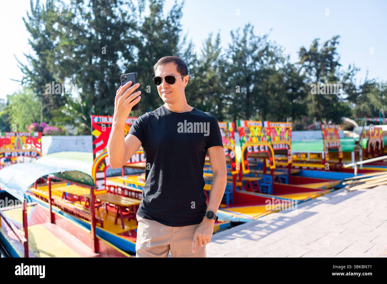Homme hispanique utilisant smartphone à Xochimilco avec des bateaux trajinera en arrière-plan, Mexico, City, Mexique Banque D'Images