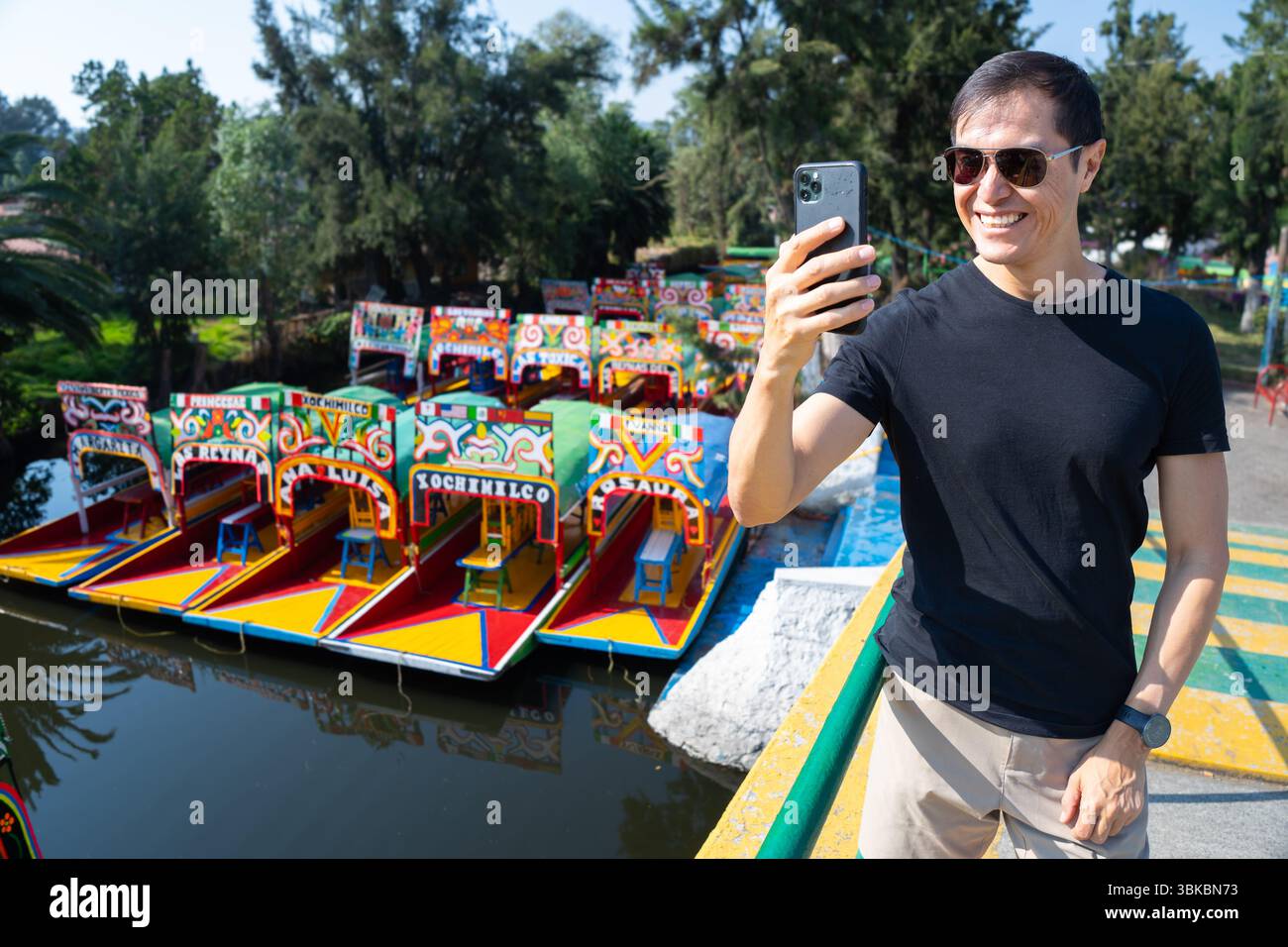 Homme hispanique utilisant smartphone à Xochimilco avec des bateaux trajinera en arrière-plan, Mexico, City, Mexique Banque D'Images