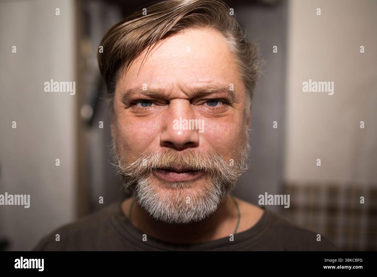 Un homme avec des poils faciaux, y compris une barbe et une moustache, grimpe son front et fait un visage drôle, mettant en valeur des rides et une expression heureuse Banque D'Images