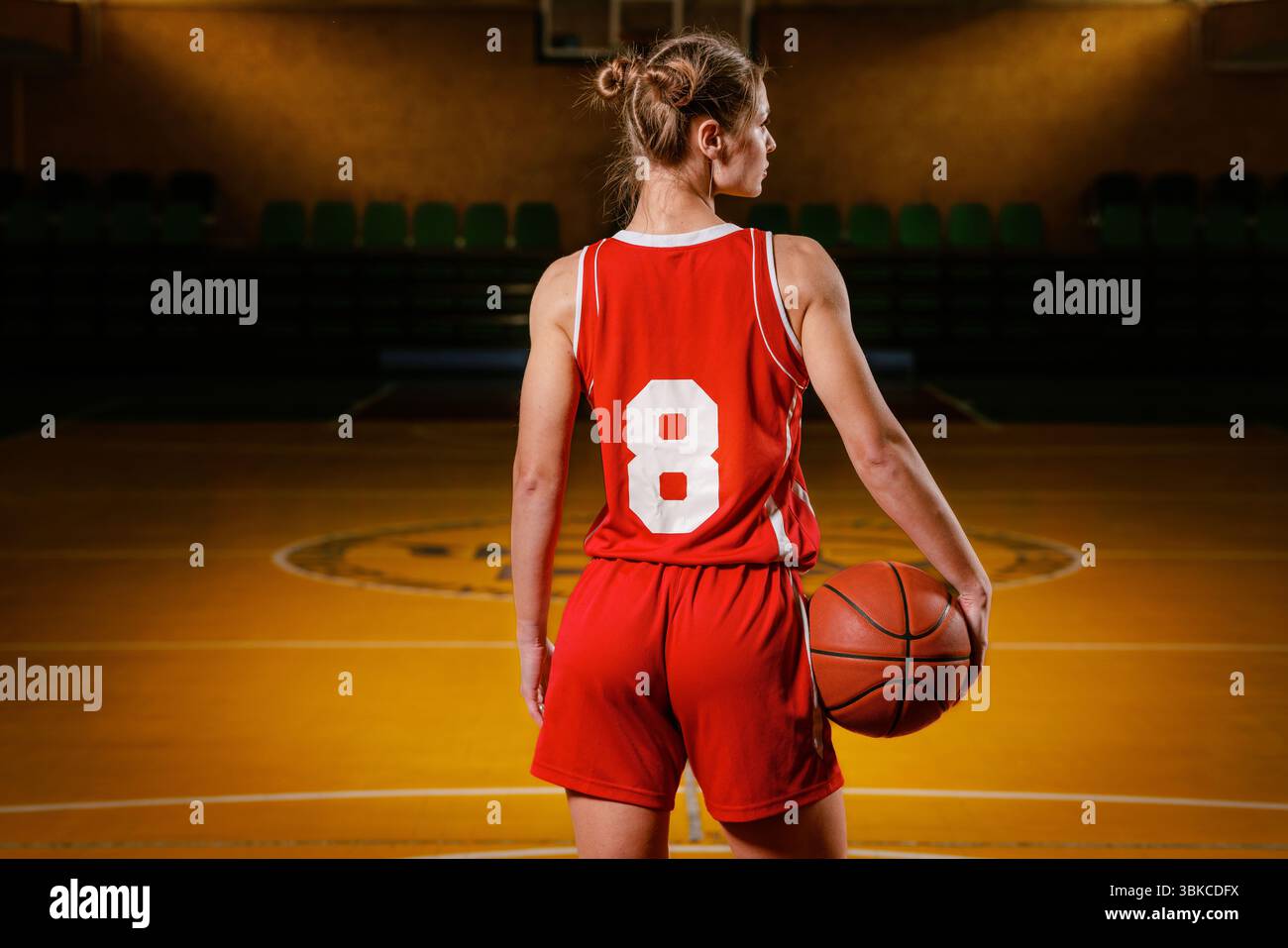 Joueuse de basket-ball en uniforme rouge tenant un ballon sur un terrain intérieur. Banque D'Images