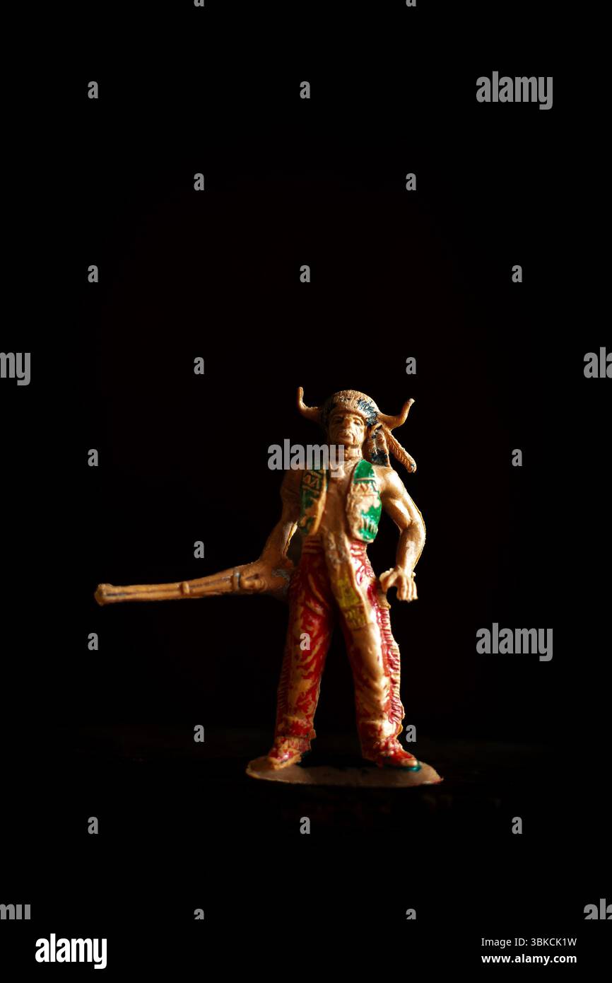 Figurine de jouet indien amérindien vintage se tient audacieusement dans un cadre sombre, brandissant une longue arme Banque D'Images