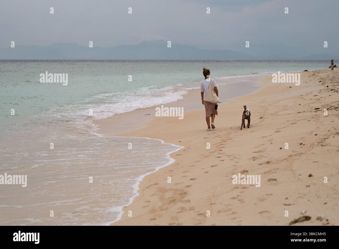 Femme marchant avec un chien le long de la plage tropicale vide à Zanzibar Banque D'Images