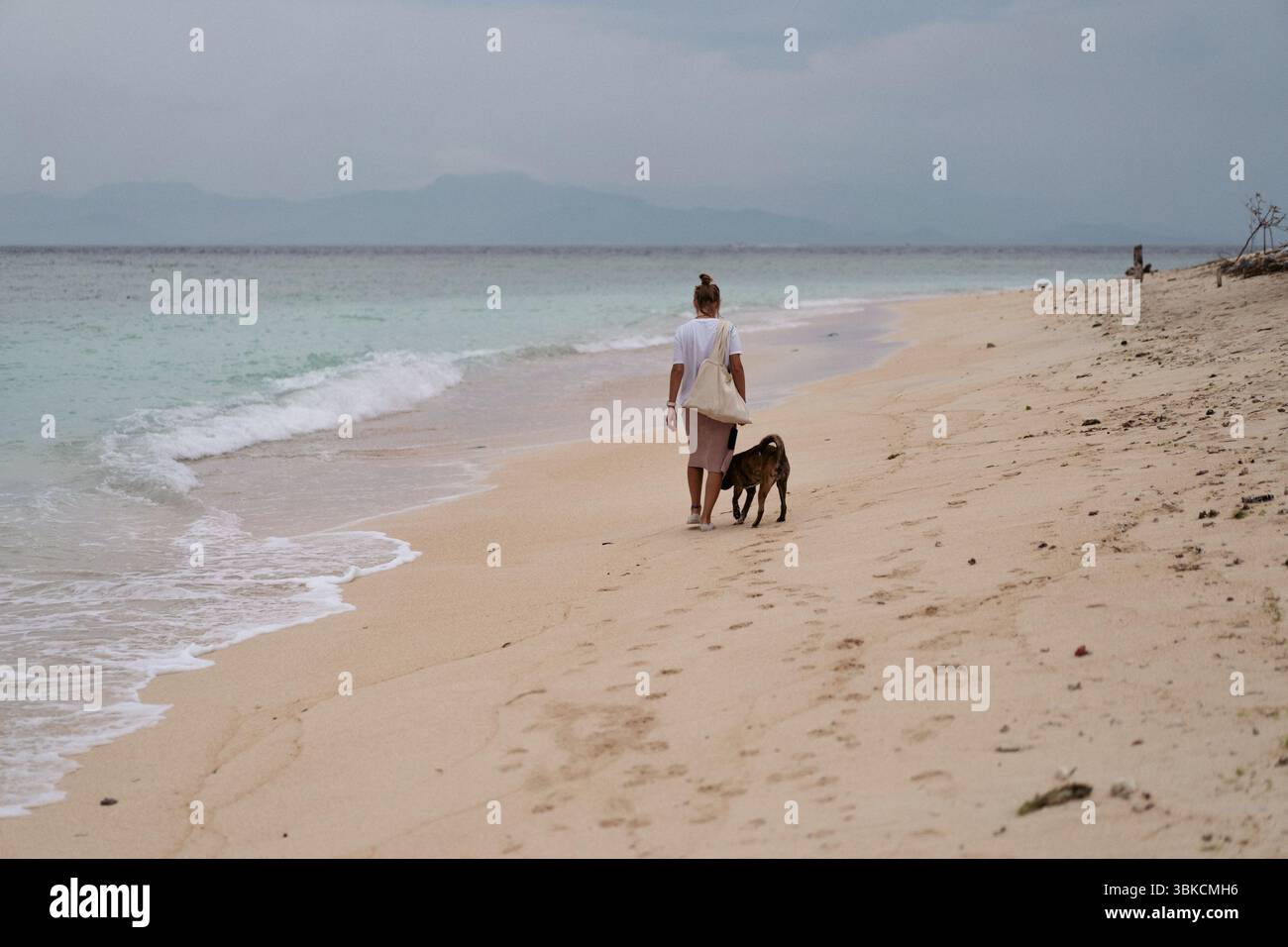 Femme marchant avec un chien le long de la plage tropicale vide à Zanzibar Banque D'Images