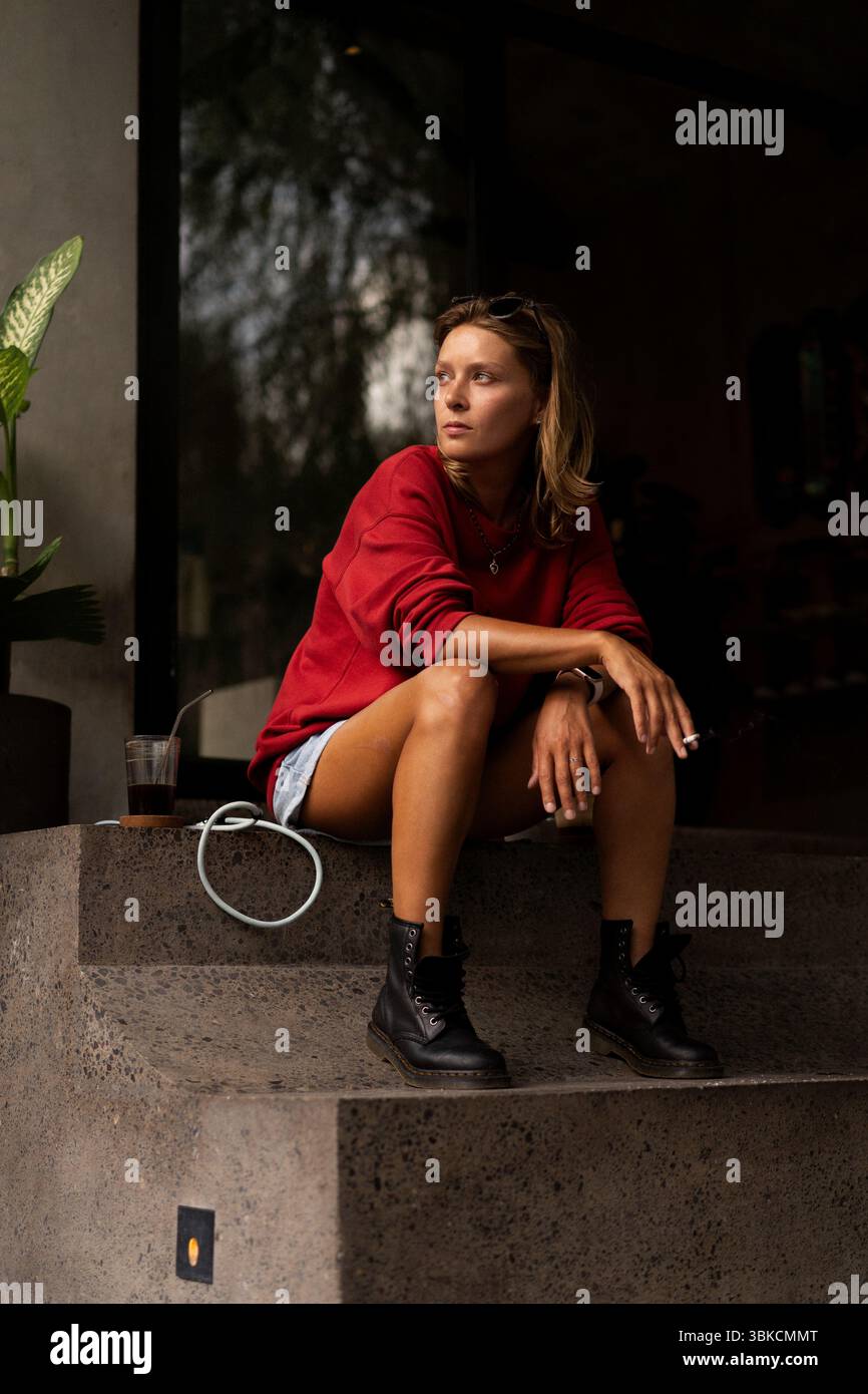 Jeune femme réfléchie assise devant le café avec café et cigarette Banque D'Images
