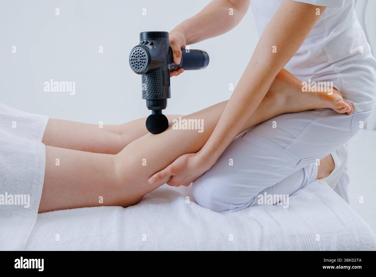 Thérapeute utilise le pistolet de massage à percussion sur les muscles du mollet des clients pour soulager la douleur, améliorer la circulation, et accélérer la récupération. Banque D'Images