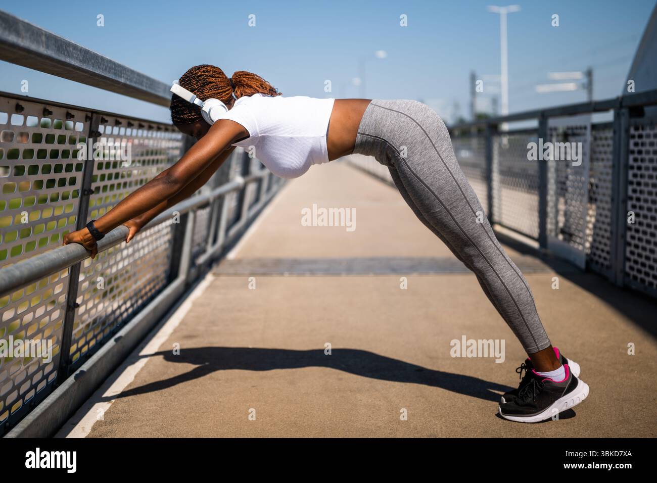 Jeune afro-américaine dans les vêtements de sport femme avec des écouteurs faisant des pompes et de l'exercice sur le pont urbain. Banque D'Images