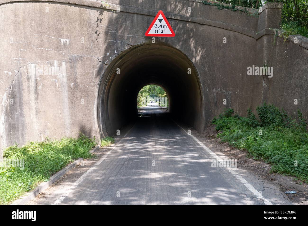 Tunnel étroit situé sous un pont en béton, avec un panneau de limite de hauteur et une lumière lumineuse visible à la fin, créant une sensation de voyage Banque D'Images