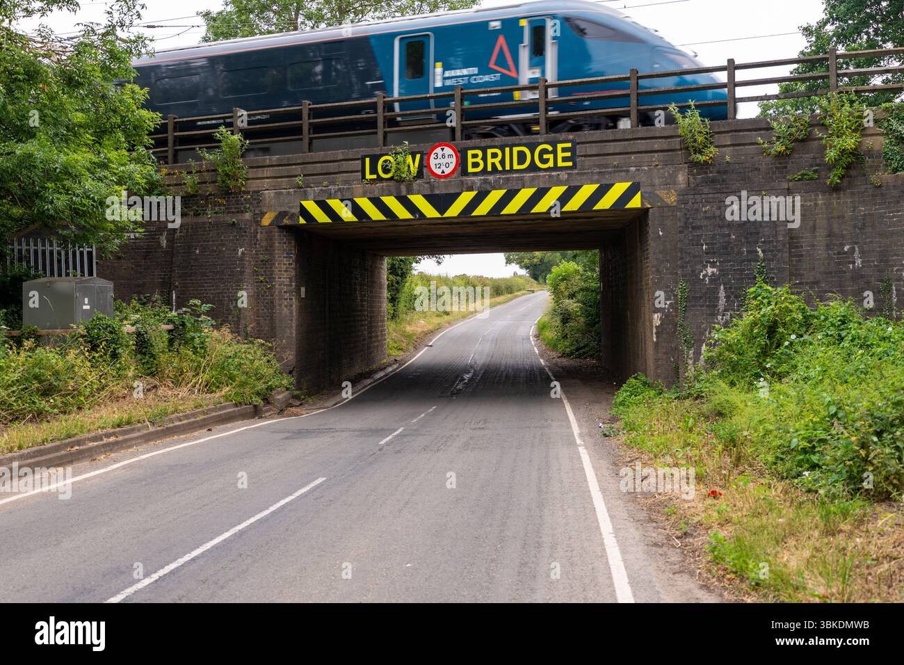Train de voyageurs glissant sur un pont bas dans la campagne pittoresque du Royaume-Uni, entouré de verdure luxuriante et de paysages ouverts Banque D'Images