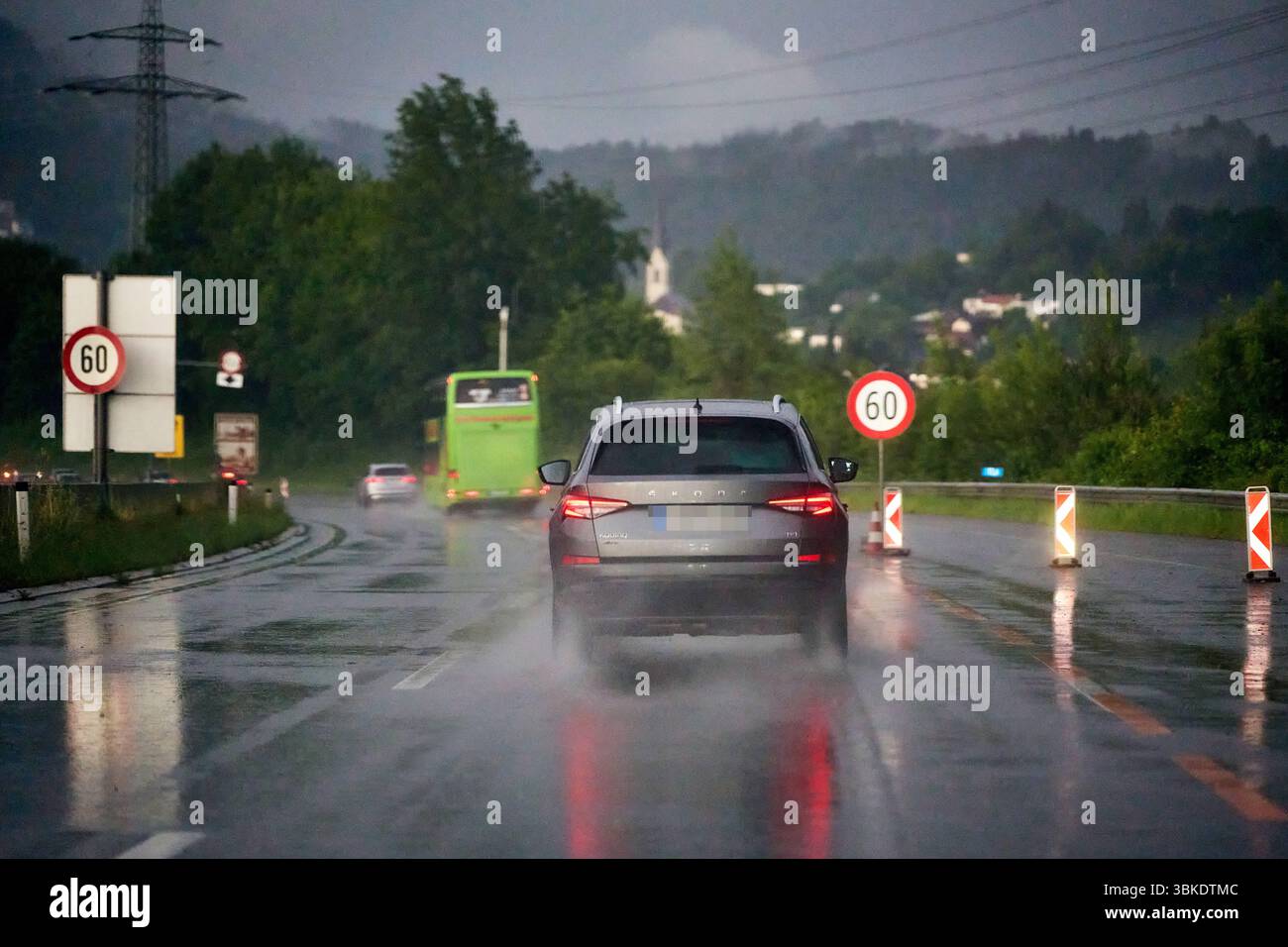 Suisse - 15 juin 2025 : véhicules circulant sur route mouillée avec une limite de vitesse de 60 km/h. Les panneaux de signalisation et les marquages avertissent les conducteurs de faire preuve de prudence dans des conditions humides et de réguler la vitesse dans des conditions de circulation dense. *** Fahrzeuge unterwegs auf regennasser Straße mit 60 km/h Tempolimit. Verkehrszeichen und Markierungen mahnen zur Vorsicht BEI Nässe und regeln die Geschwindigkeit im dichten Verkehr. Banque D'Images
