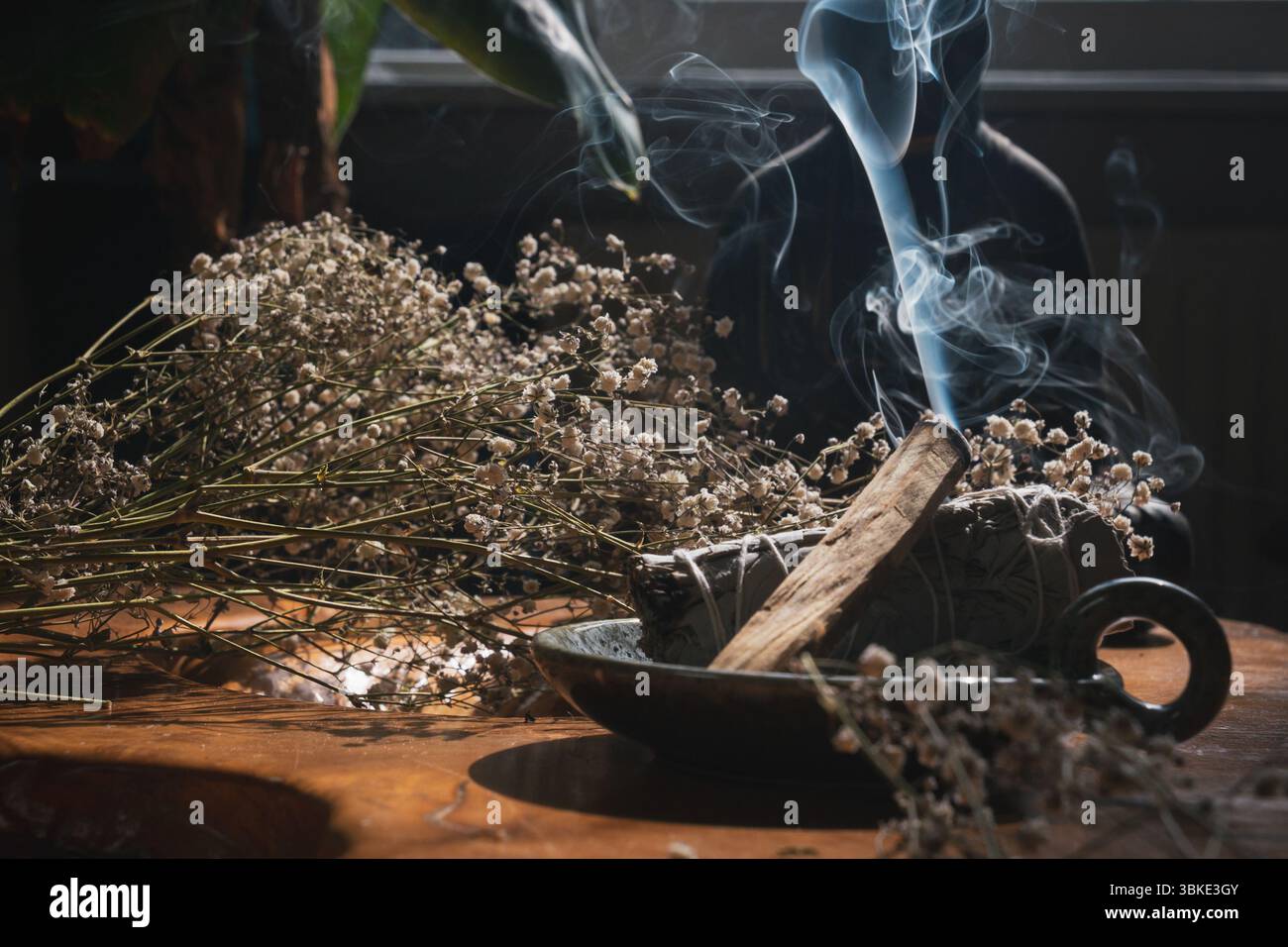 Palo Santo et la sauge brûlent de fumée visible, entourés de fleurs séchées sur une table en bois Banque D'Images