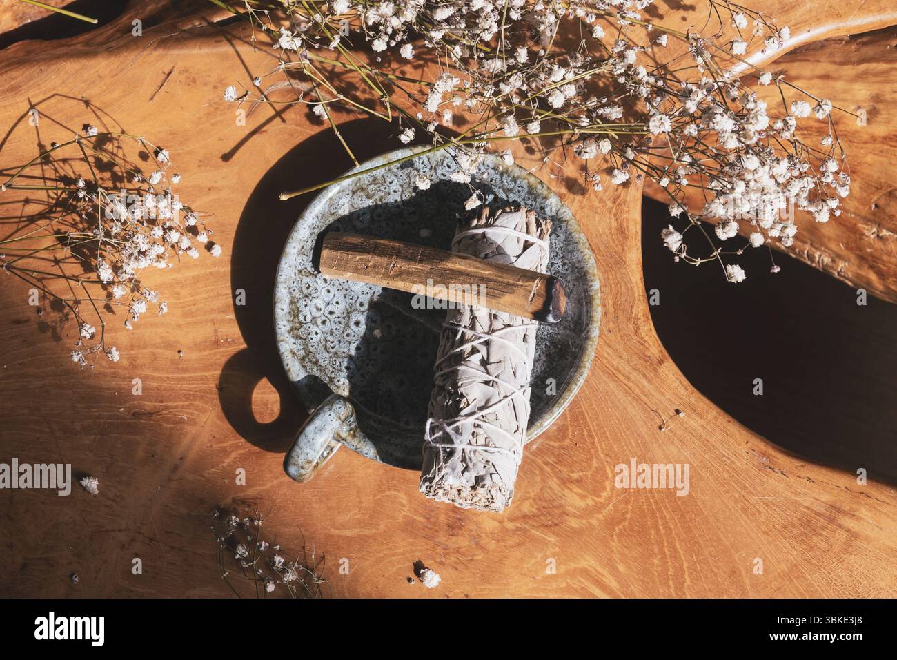 Bâtonnet de sauge et bois de Palo Santo dans un bol en céramique, entouré de fleurs sur une surface en bois Banque D'Images